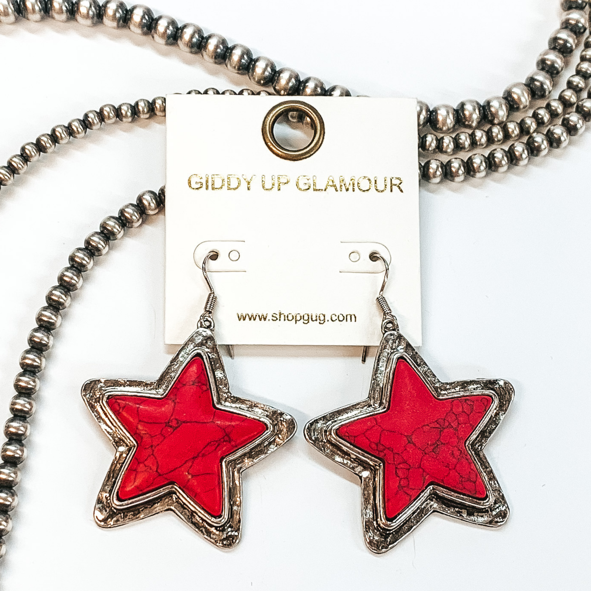 Red stone star dangling earrings with silver lining, pictured on a white background and beaded decor.  