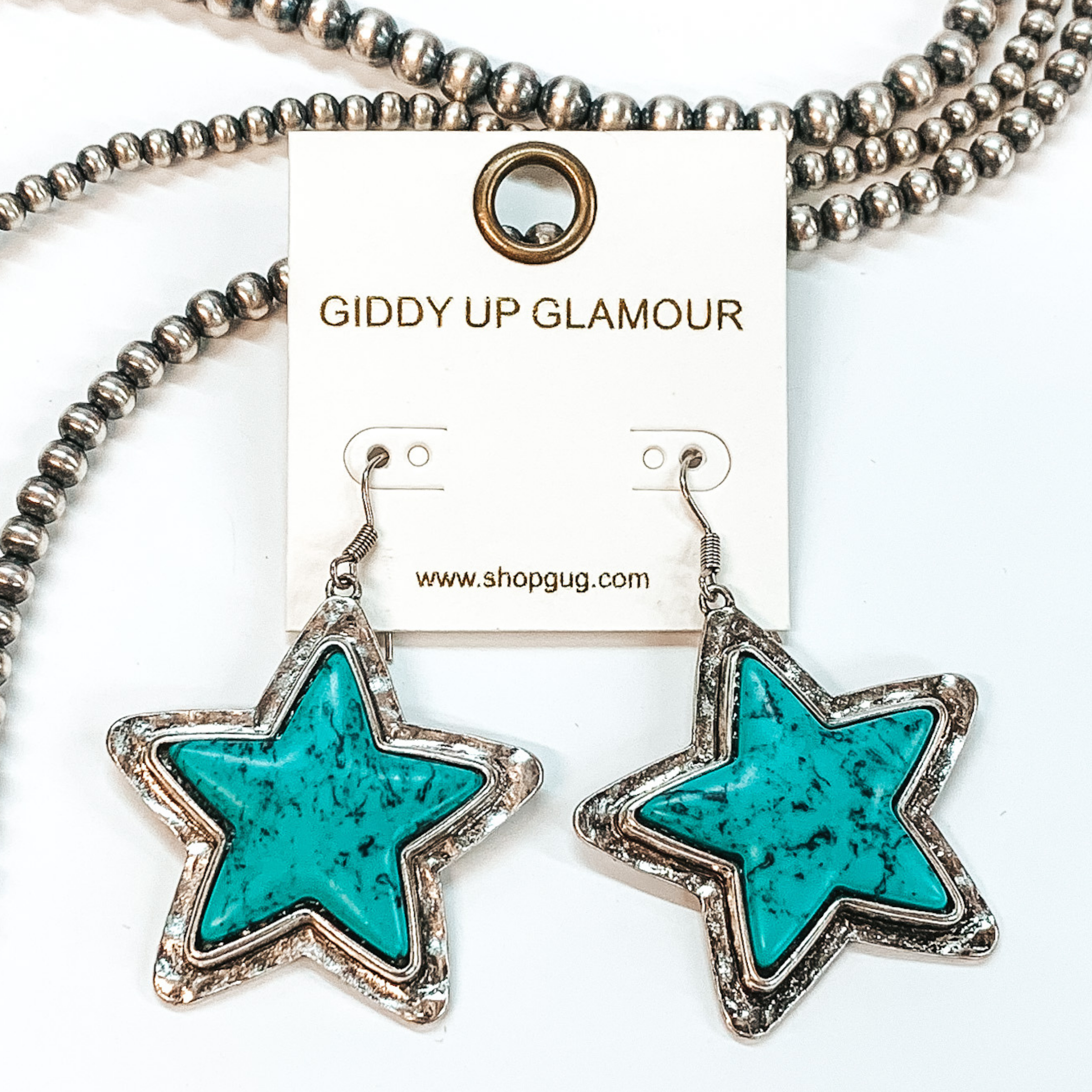Turqouise stone star dangling earrings with silver outline, pictured on a white background and beaded decor.  