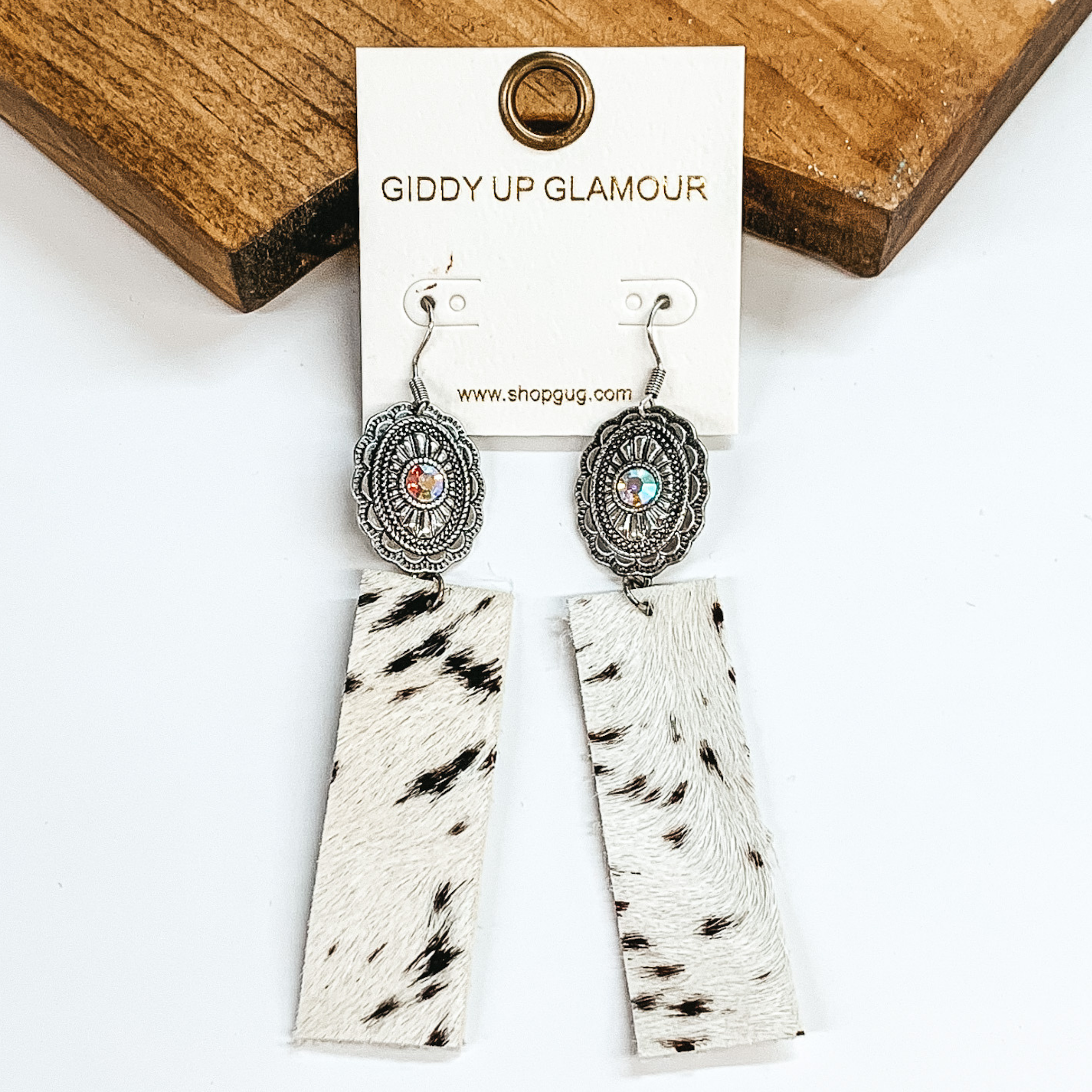 Silver concho with AB crystal in the center and faux  black and white rectangle cow hide earrings. Pictured in a white background with a brown block.