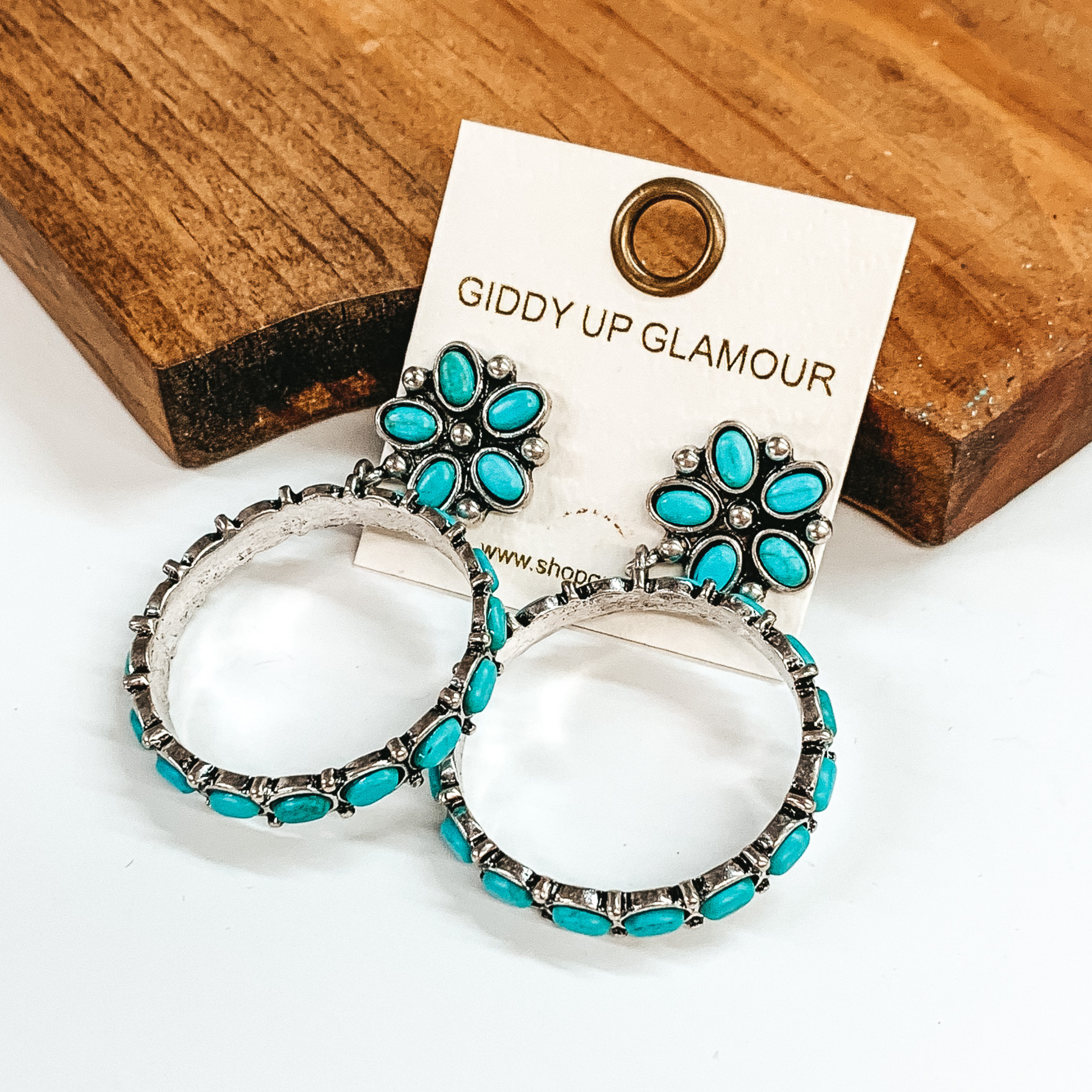 Turquoise flower post earrings outlined in silver and circle drop pendant with turquoise stones around. Pictured in a brown block and white background.