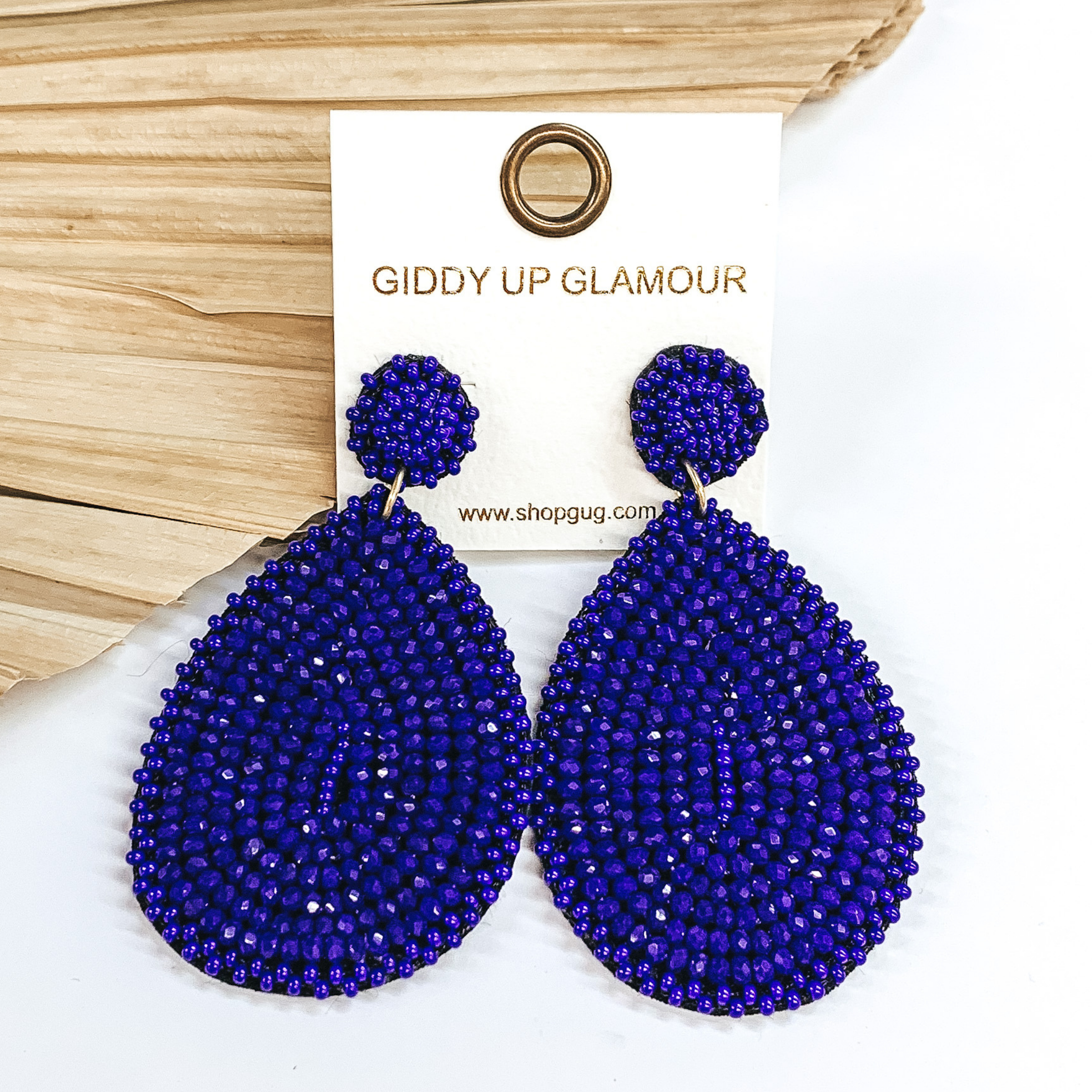 Blue beaded drop earrings in a teardrop shape. These earrings are pictured on a white background with a dried palm leaf in the background.