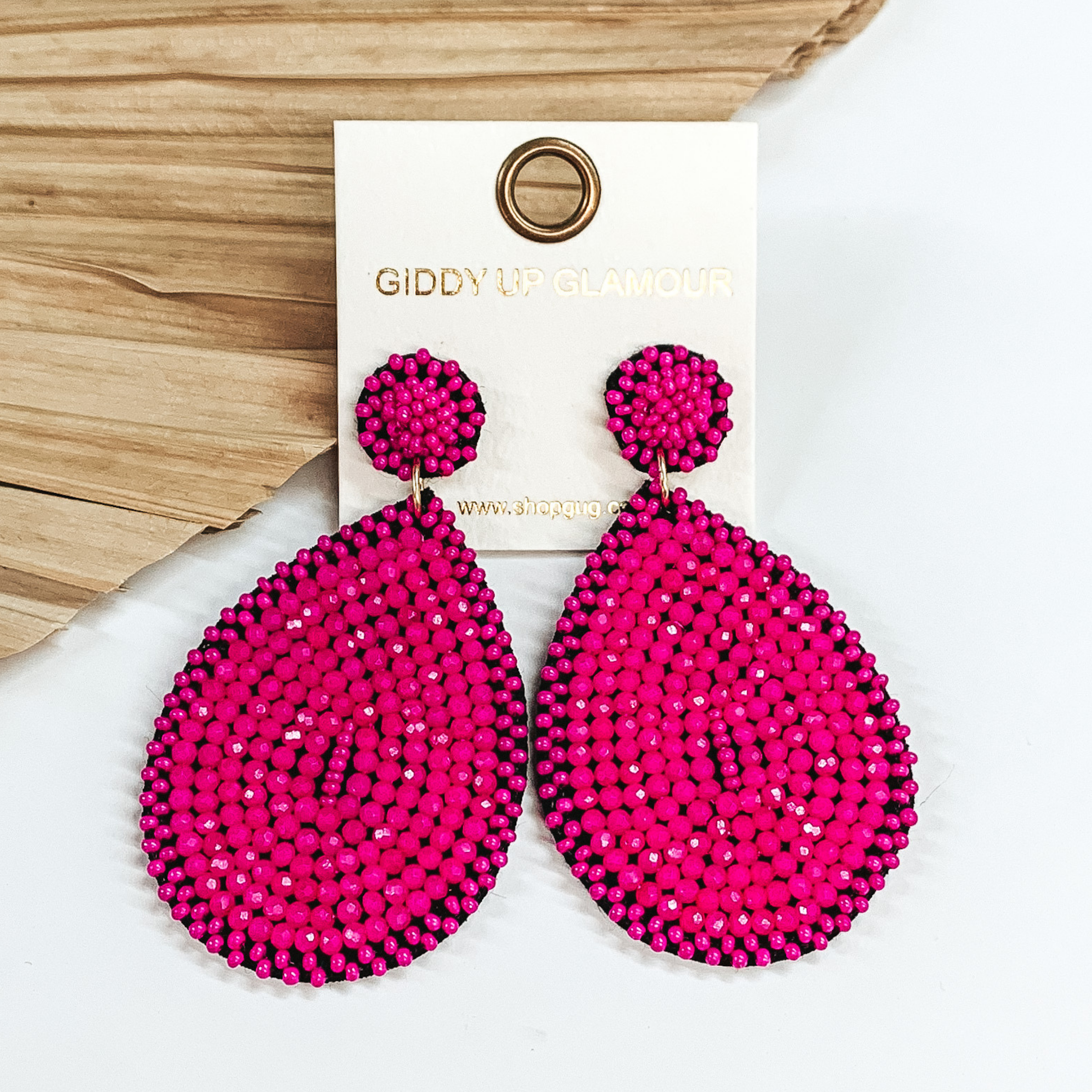 Pink beaded drop earrings in a teardrop shape. These earrings are pictured on a white background with a dried palm leaf in the background.