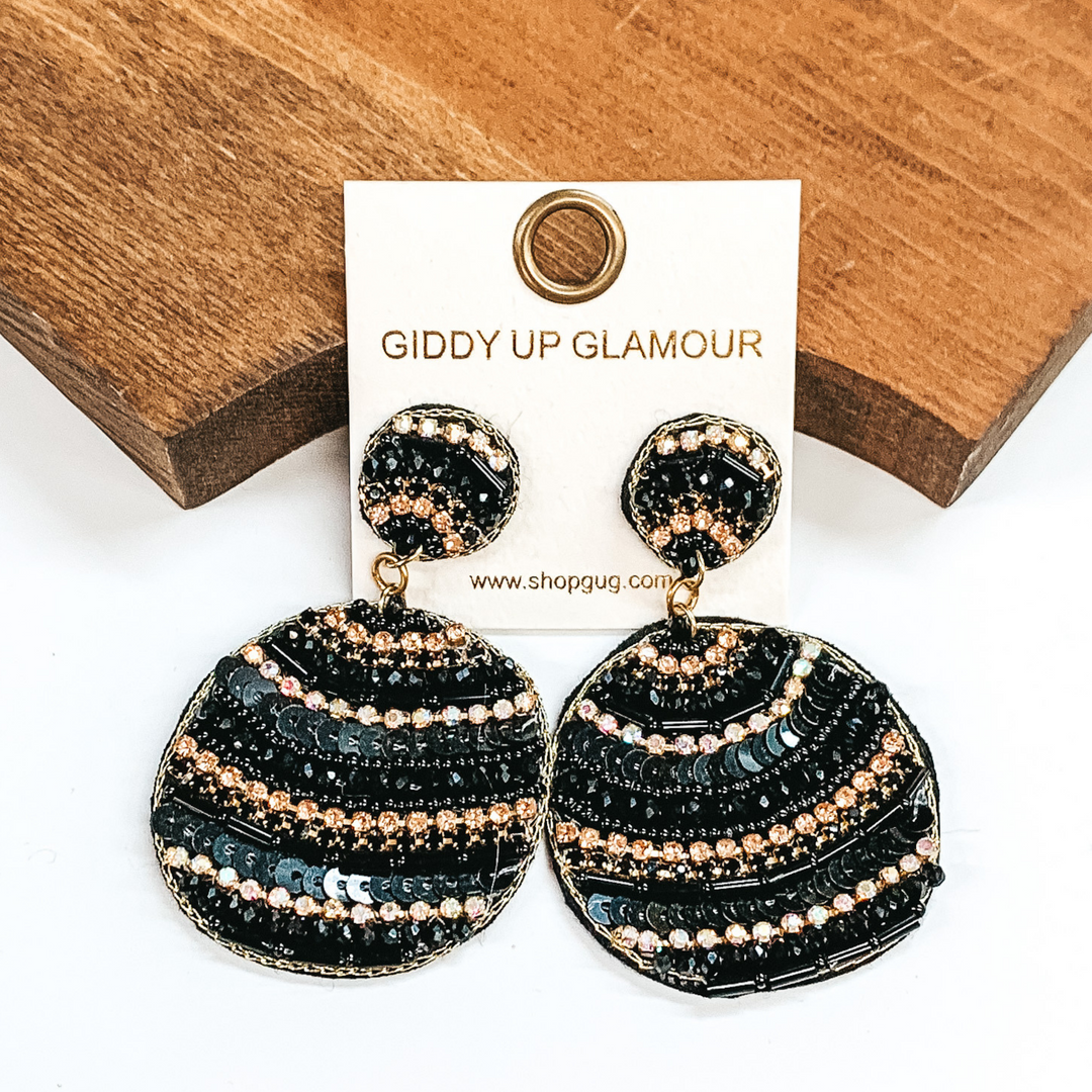 Black cirle drop earrings with different striped beaded patterns. Striped patterns in long and small  black beads, black sequins, with ab, black, and gold crystals. Taken in a white  background with a brown block as decor.
