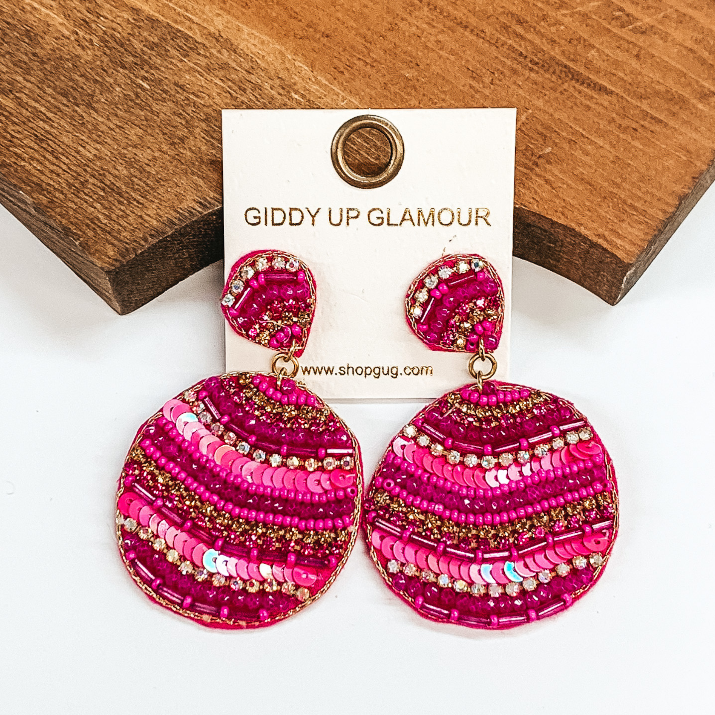 Pink cirle drop earrings with different striped beaded patterns. Striped patterns in long and small  pink beads, pink sequins, with ab, pink, and gold crystals. Taken in a white  background with a brown block as decor.