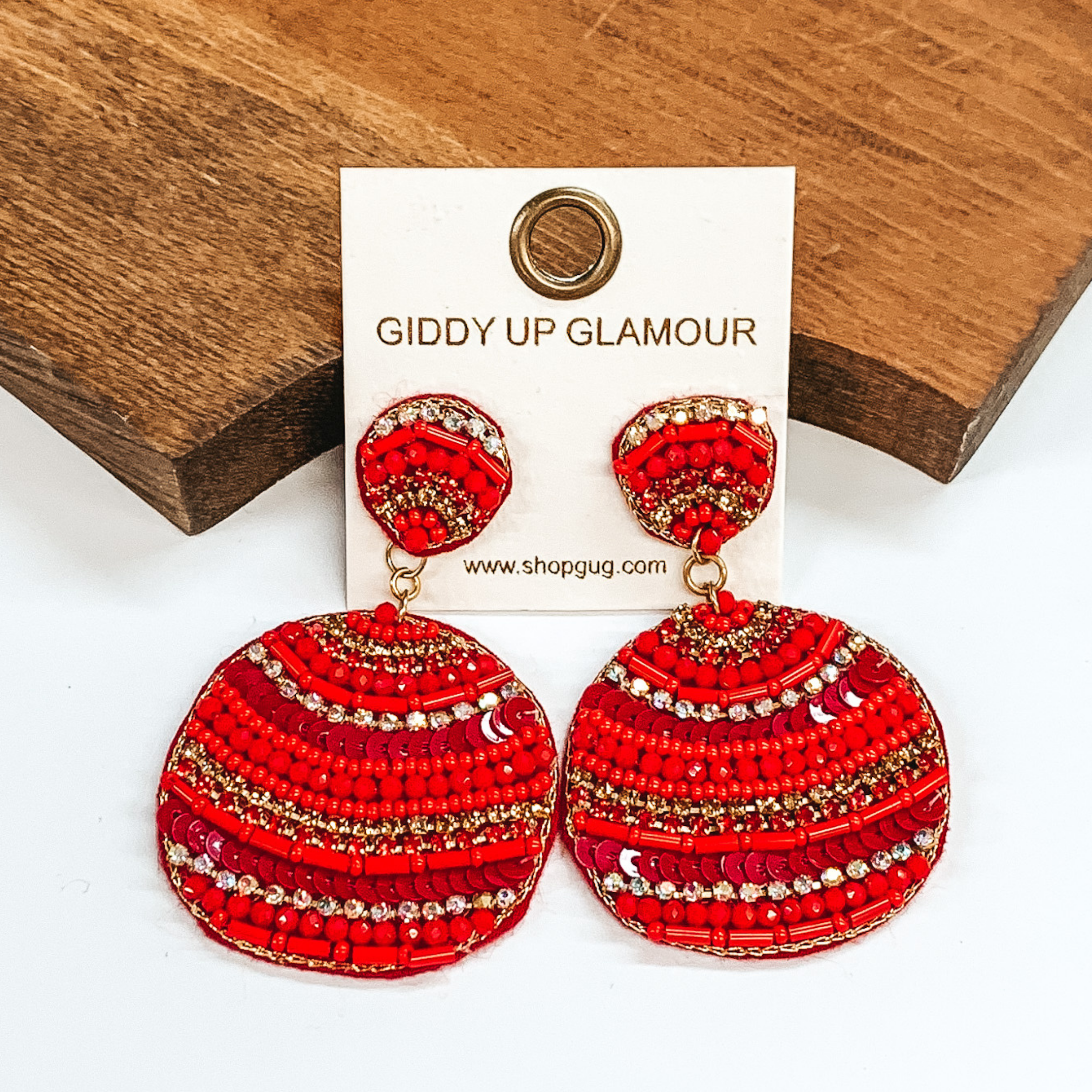 Red cirle drop earrings with different striped beaded patterns. Striped patterns in long and small  red beads, red sequins, with ab, red, and  gold crystals. Taken in a white background with a  brown block as decor.
