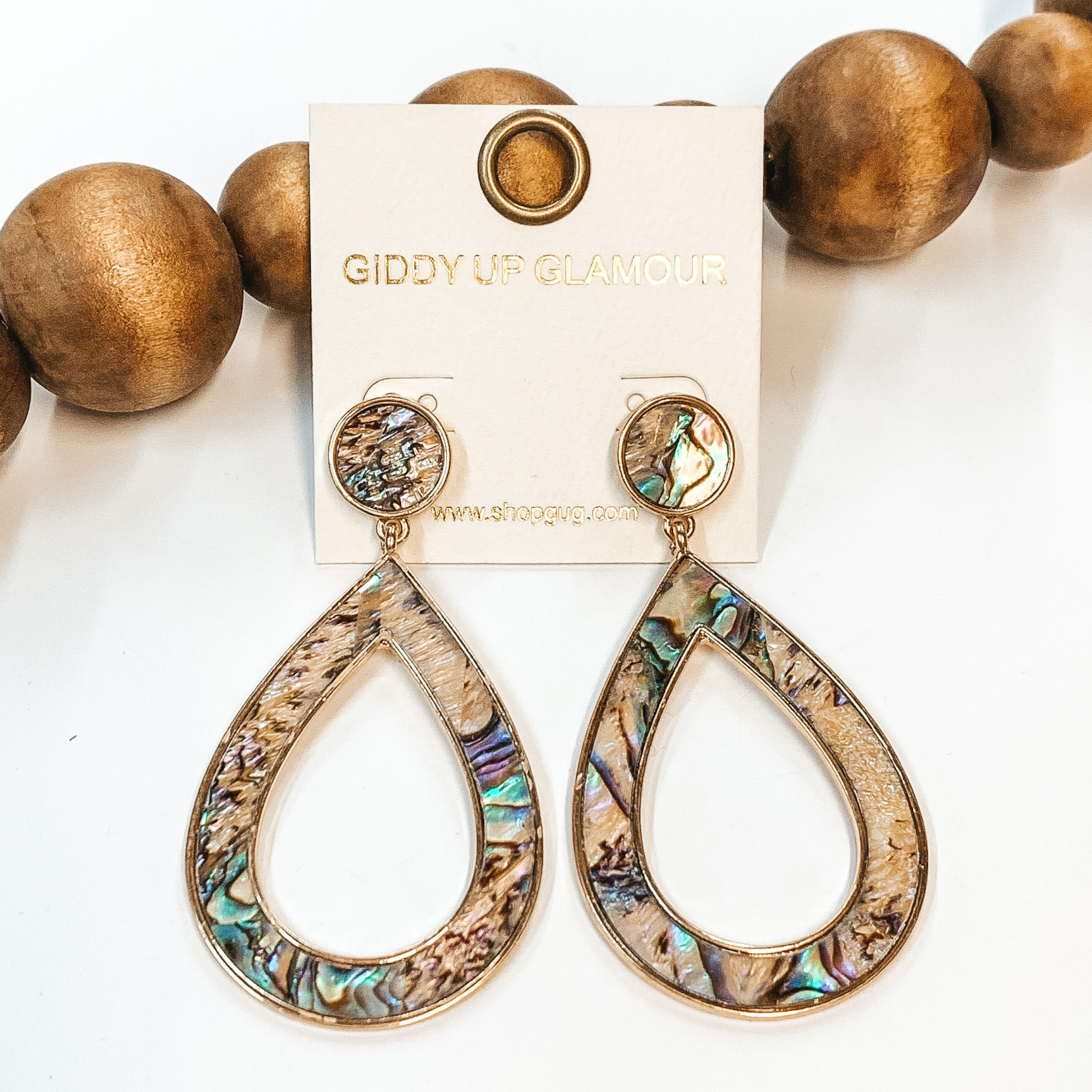 Open teardrop earrings in abalone shell with  gold outline. Taken in a white background with  brown beads as decor.
