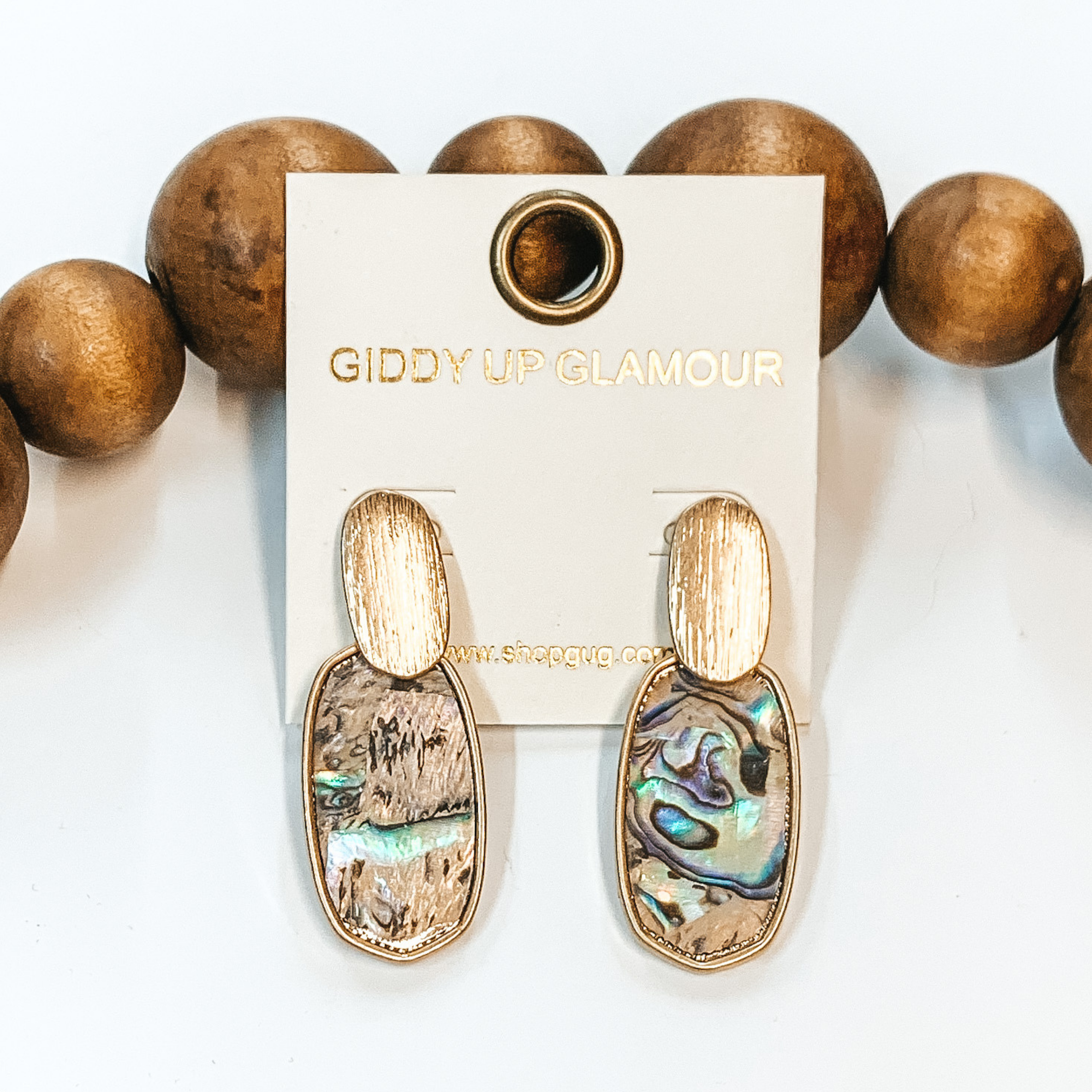 Abalone shell oval shaped earrings with gold  outline and gold accents. Taken in a white background with brown beads as decor.