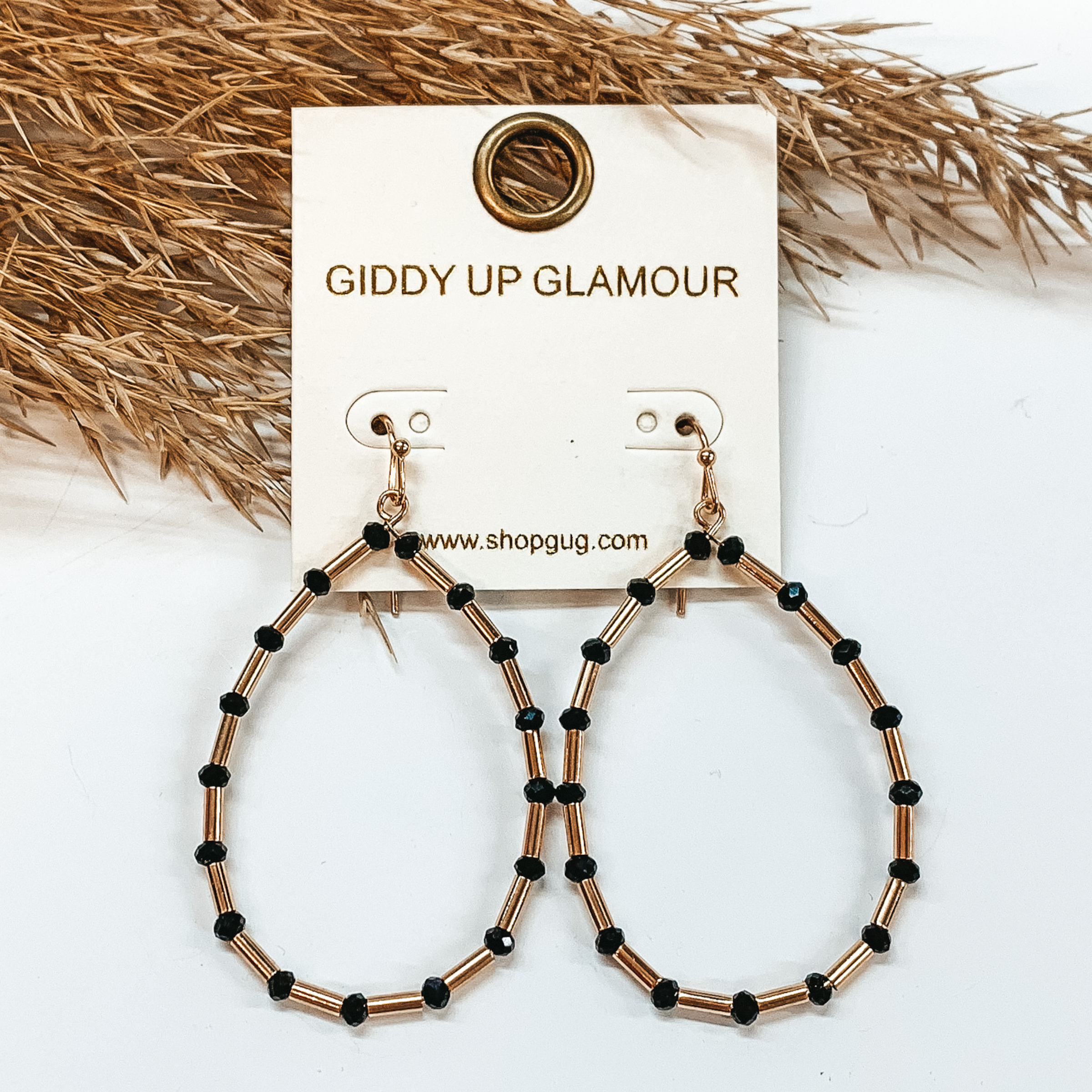 Teardrop earrings with long gold beads and black beads. Taken in a white  background with a brown plant as decor.