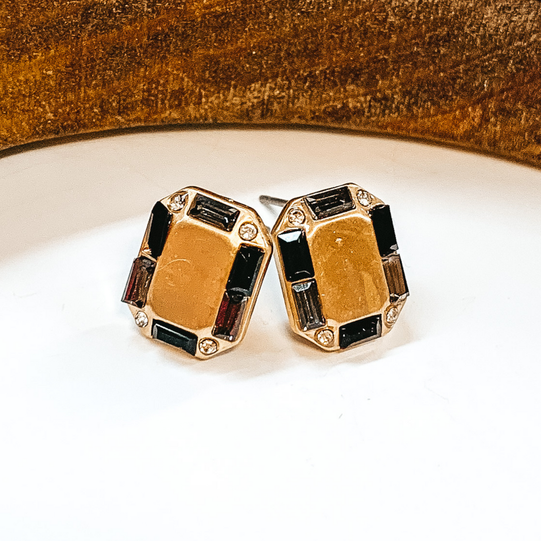 Gold rectangle shaped earrings with a black  crystal outline. Small black crystals in different  tones. Taken on a white background with a brown  block in the back.