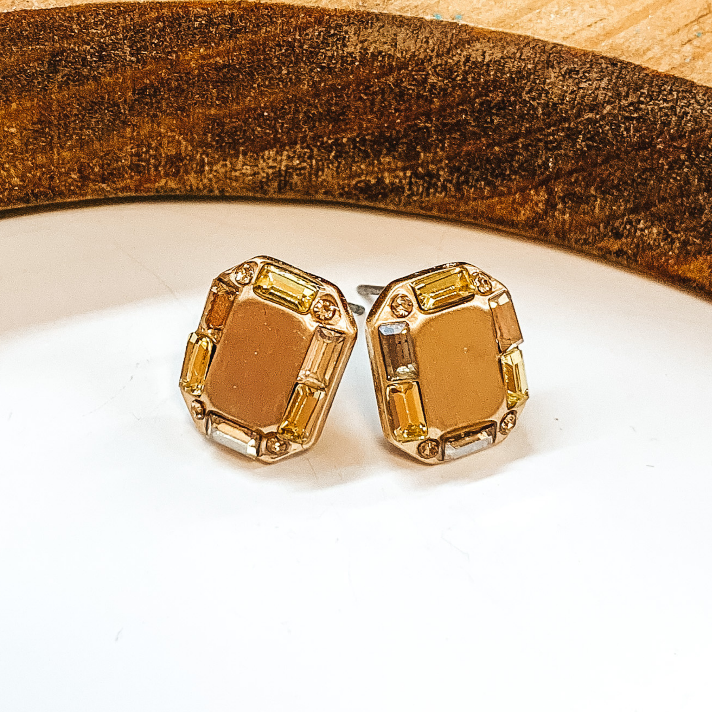 Gold rectangle shaped earrings with a yellow  crystal outline. Small yellow crystals in different  tones. Taken on a white background with a brown  block in the back.