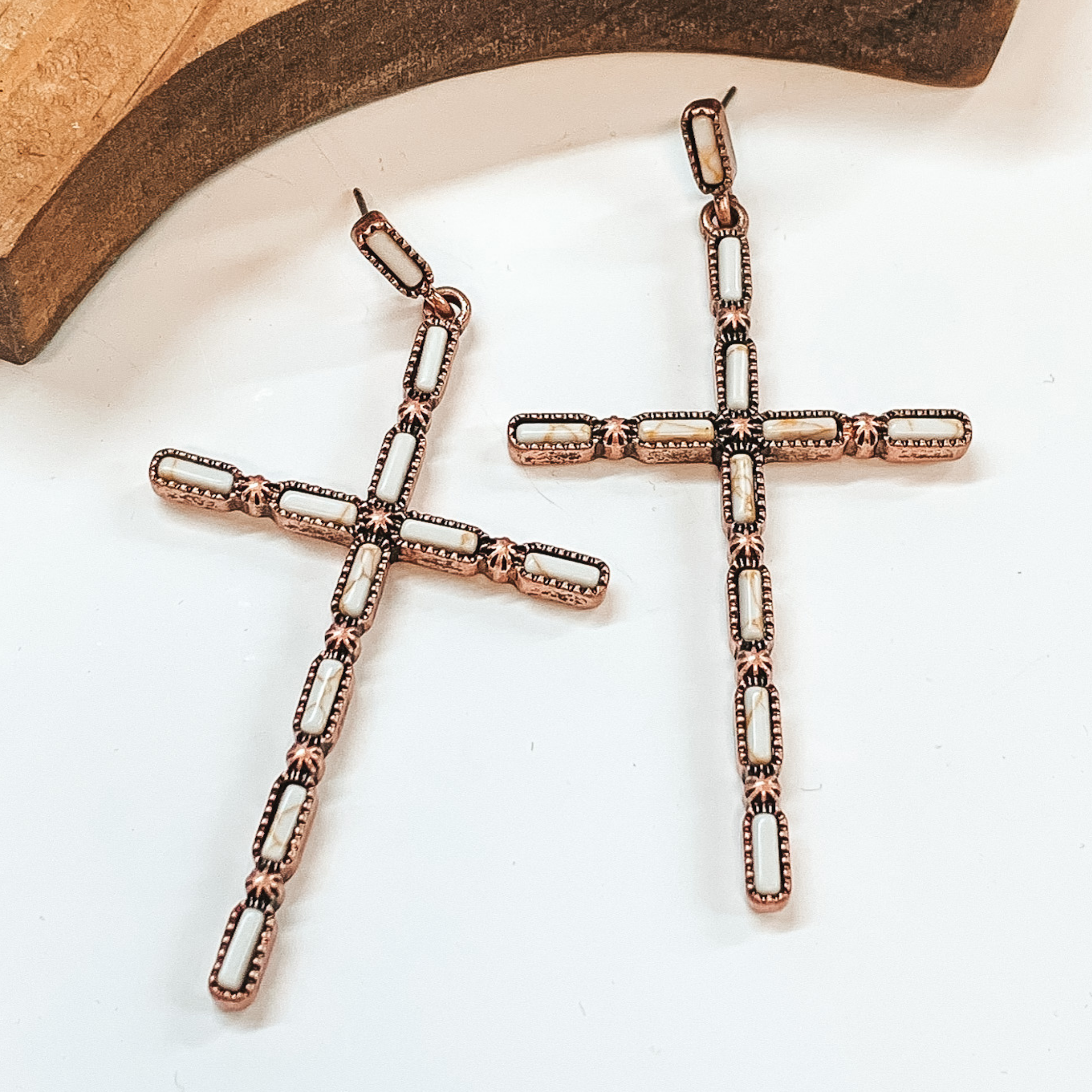 Copper cross earrings with rectangle, ivory  stones and small silver star-like details.    Taken in a white background with a brown block in the back.