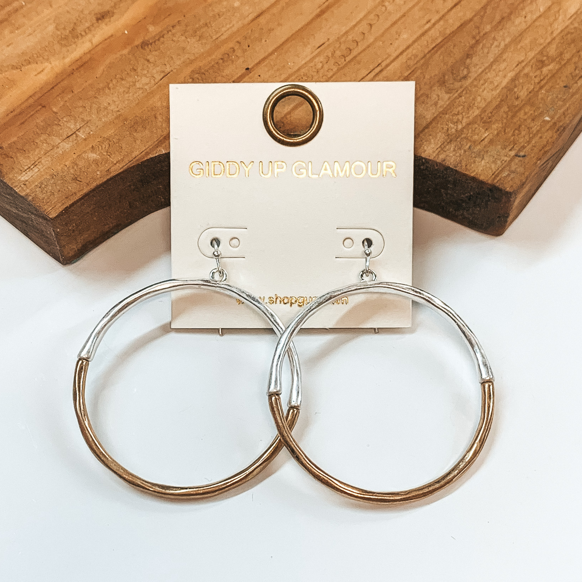Two toned circle drop earrings with hammered texture. Top half in silver and bottom half in gold. These earrings are pictured on a white background with a brown block in the back.