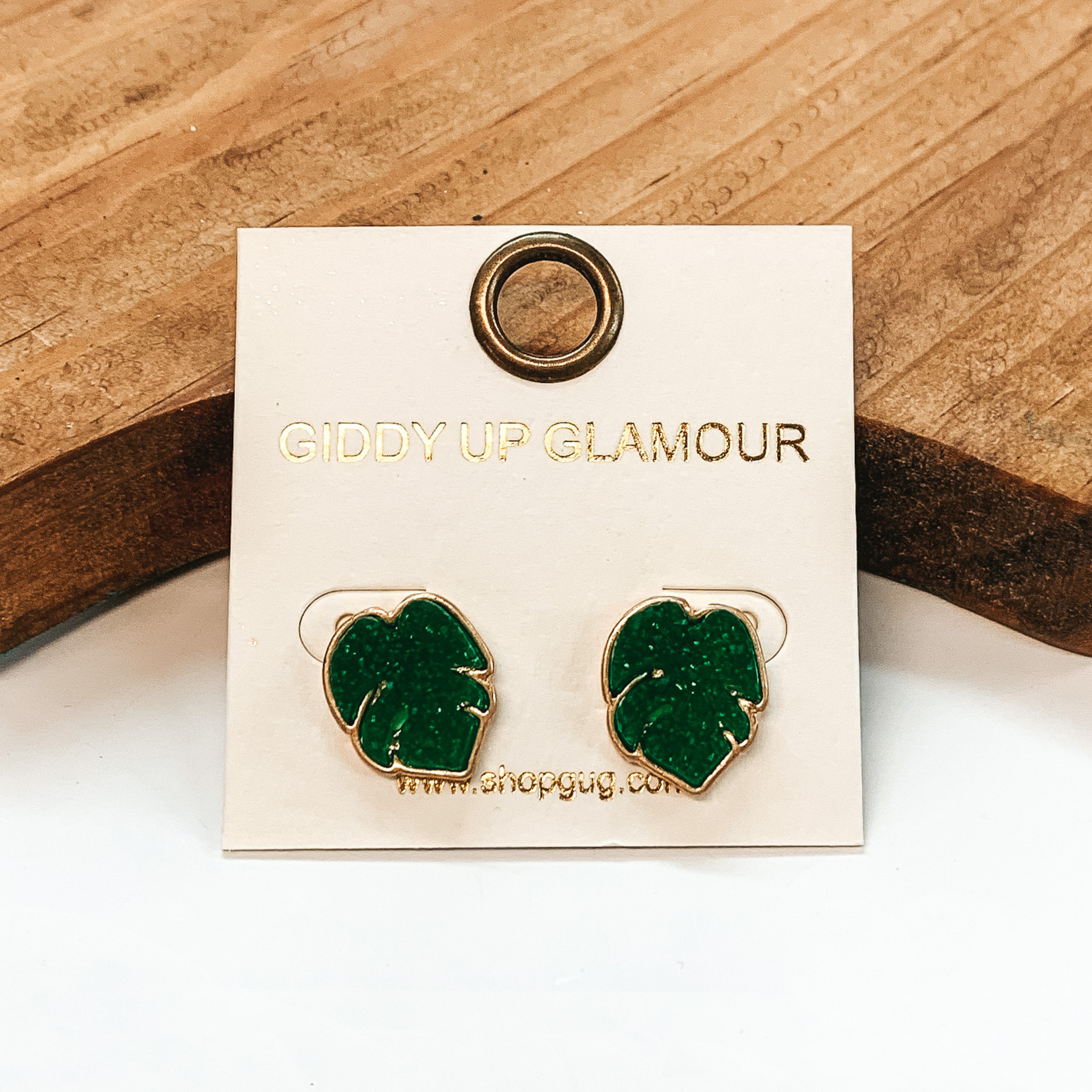 Gold post back earrings with green druzy, palm leaf shape stone. Taken on a white  background and brown block in the back.