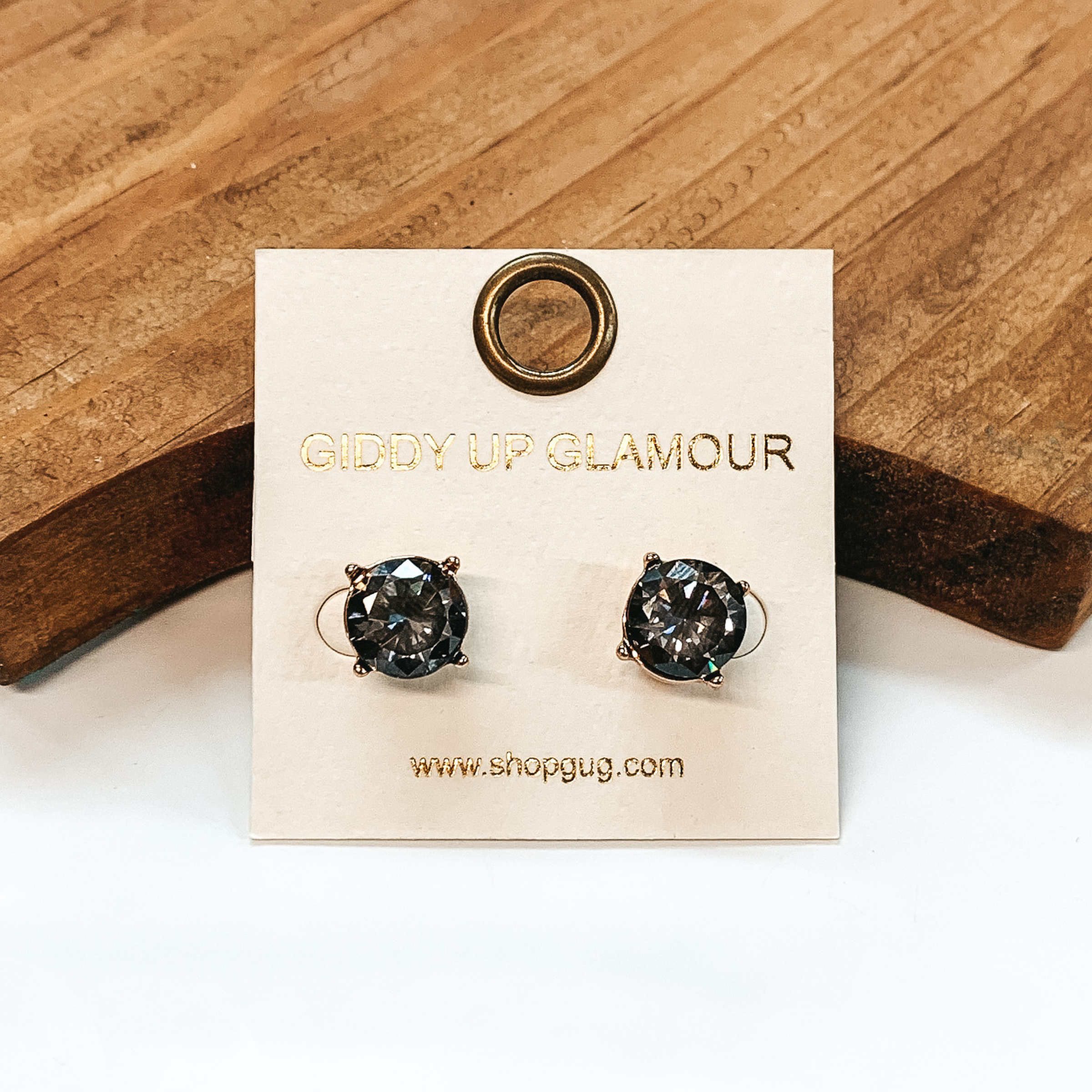 Gold setting stud earrings with CZ dark gray crystal. These earrings are pictured on a white background with a brown block in the back.