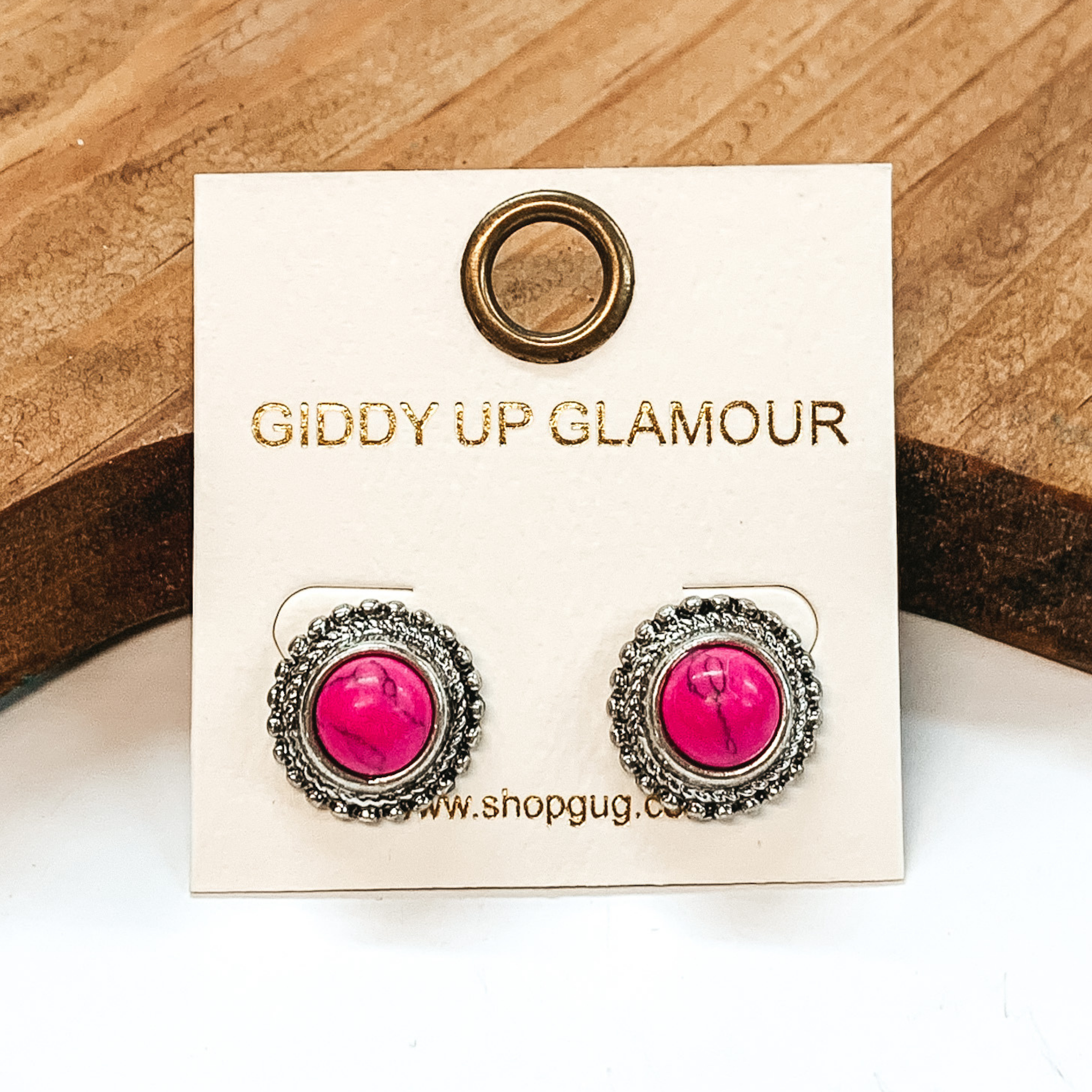 Studded earrings with silver outline with a pink stone in the middle. These earrings are pictured on a white background with a brown block in the back.