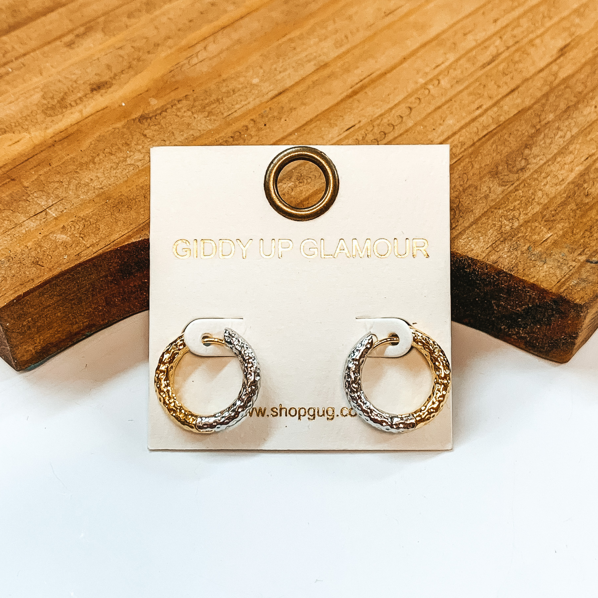 Small hammered textured hoops in half silver and  gold. These earrings  are pictured on a white background with a brown block in the back.