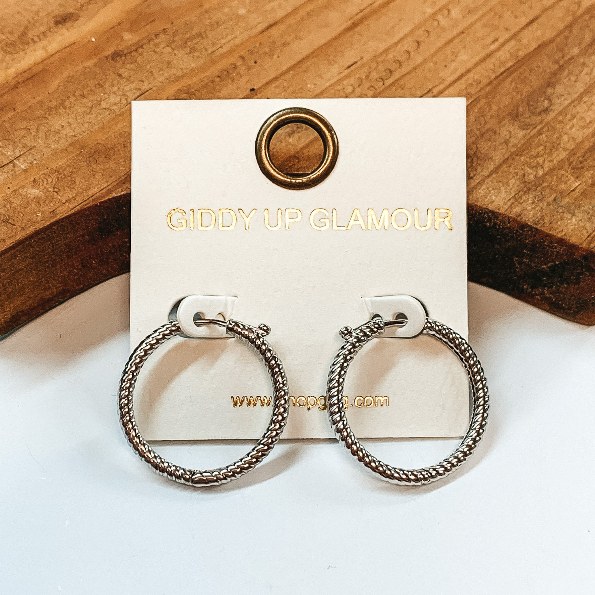Small silver hoop earrings with rope texture. Taken on a white background with a brown block in the back.