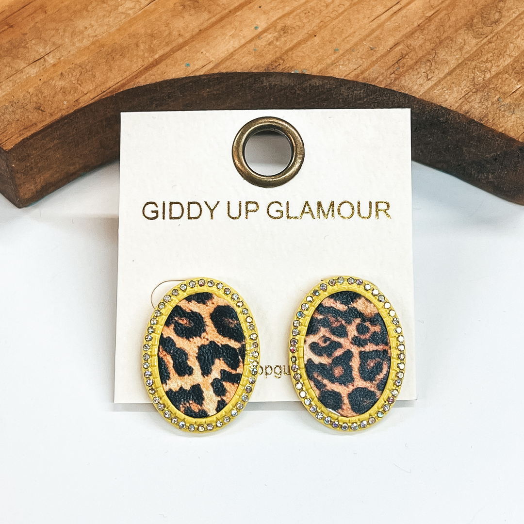 Neon yellow oval post back earrings with small  AB crystals all around. Leopard print in an oval  shape in the middle. These earrings  are pictured on a white background with a brown block in the back.