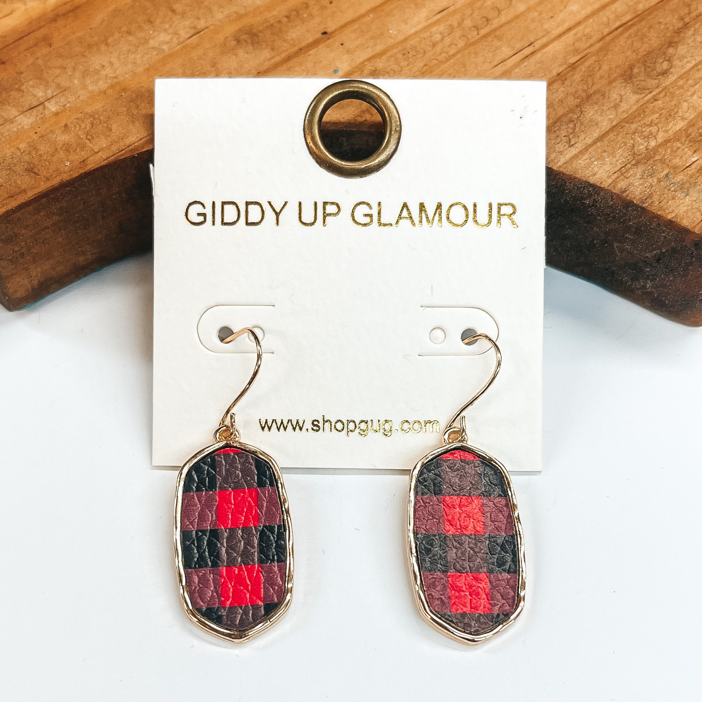 Rectangular earrings with gold setting in  red and black plaid. Taken in a white background  with a brown block in the back.