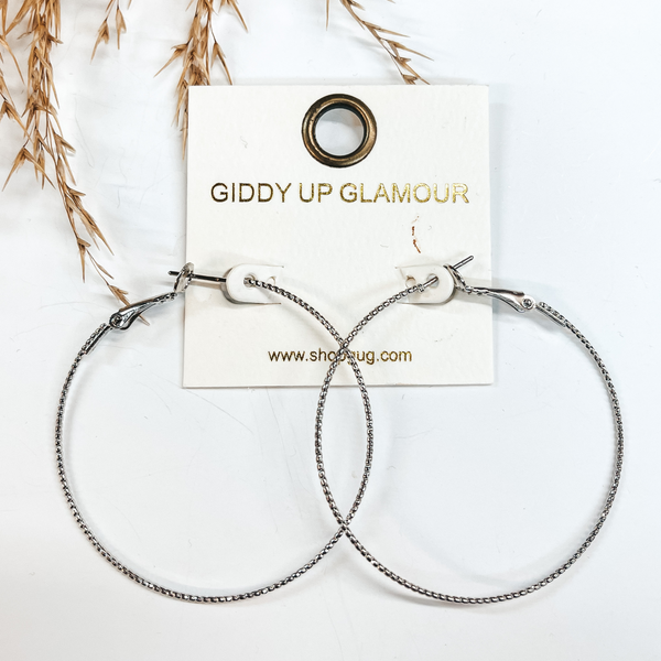 Thin wired silver hoops with rope texture.  Taken on a white background with a brown plant in the back as decor.