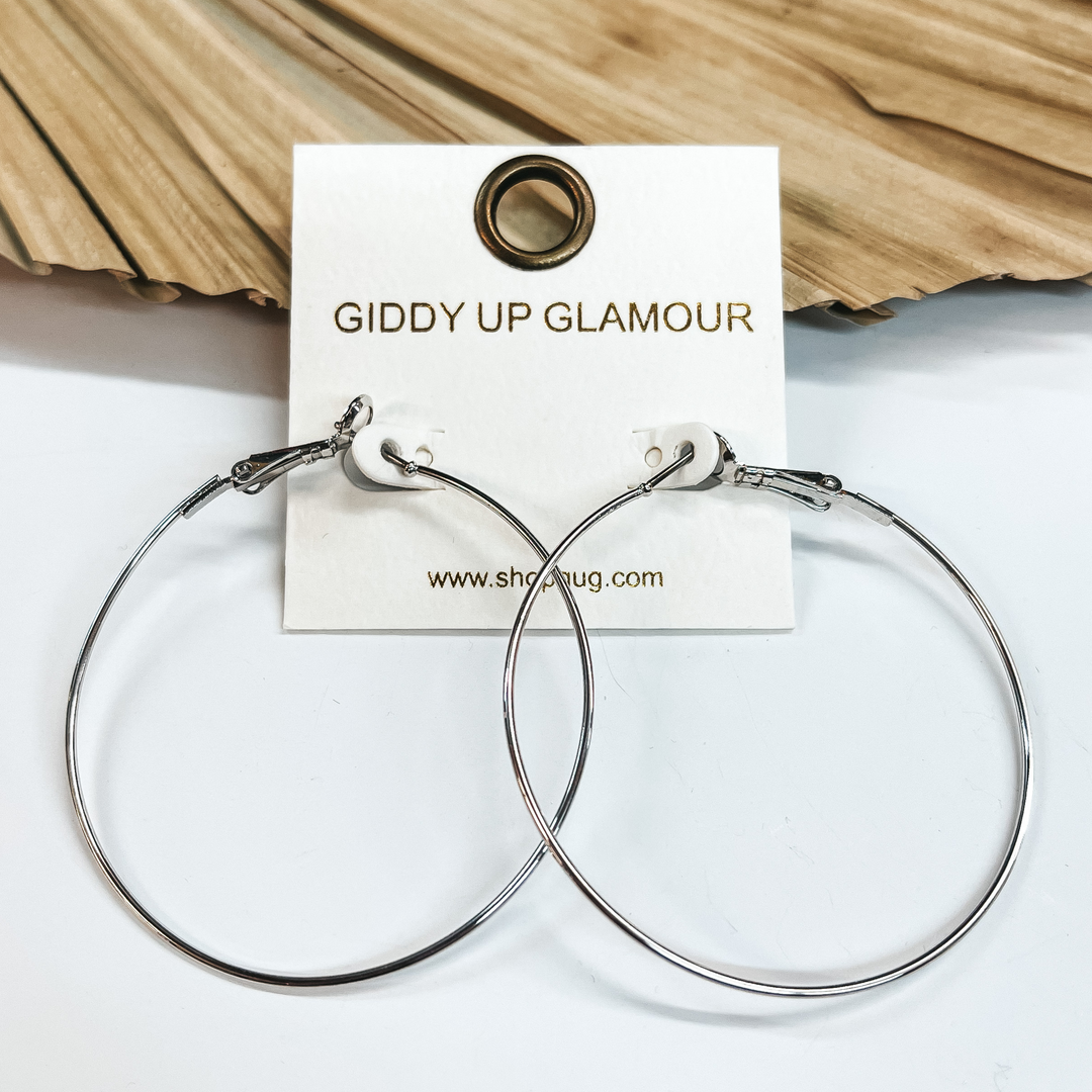 Simple thin wired hoop earrings in silver  with a saddleback backing. Taken on a white background and leaned up against a  dried up palm leaf.