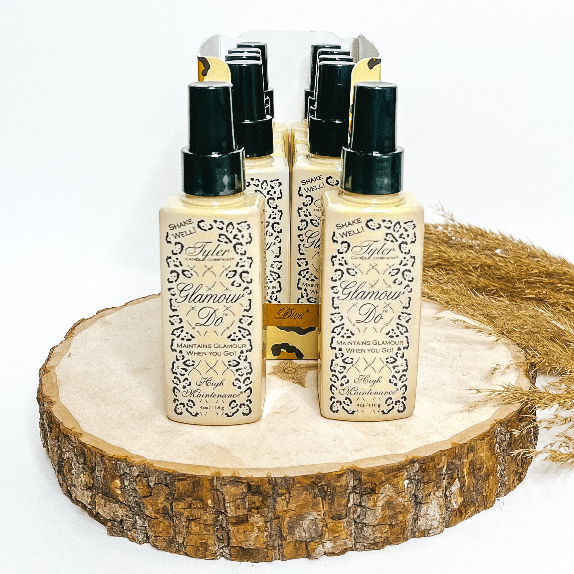 Tyler Candles Glamour Do pictured in Diva and High Maintenance scents in 4 oz size bottles with Tyler logo and leopard print design on the bottle.  Bottles are sitting on top of tree log piece with pampas grass in background.