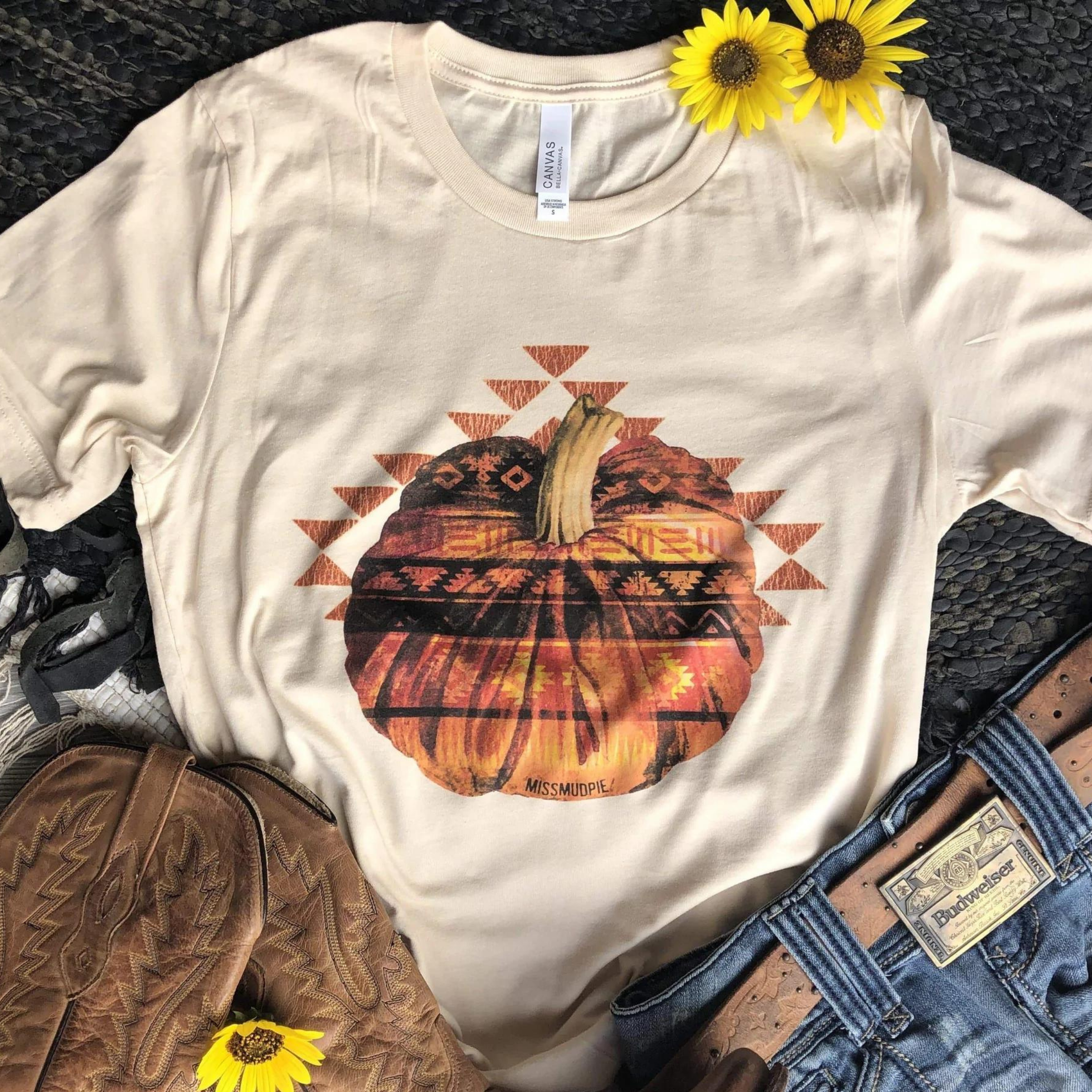 This is a cream colored tee with an Aztec designed pumpkin. Surrounding the pumpkin is several many triangles. This top is pictured with some blue jeans and brown cowgirl boots along with two little sunflowers.