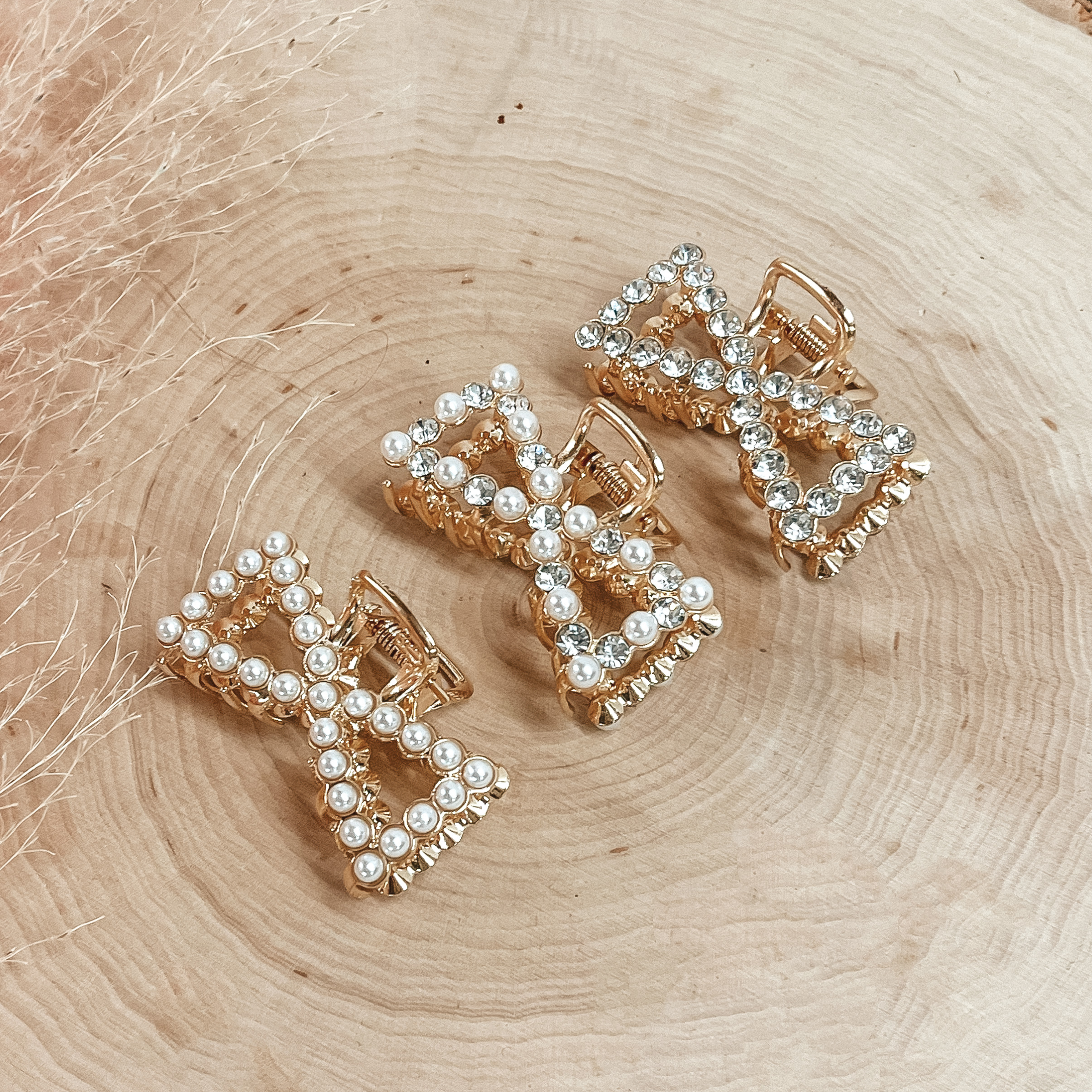 Pictured on a piece of wood are three bow claw clips. One clip has all clear crystal outline, one clip has white pearl and clear crystal outline, and the last clip has all white pearl outline. 