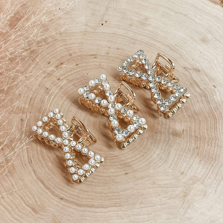 Pictured on a piece of wood are three bow claw clips. One clip has all clear crystal outline, one clip has white pearl and clear crystal outline, and the last clip has all white pearl outline. 