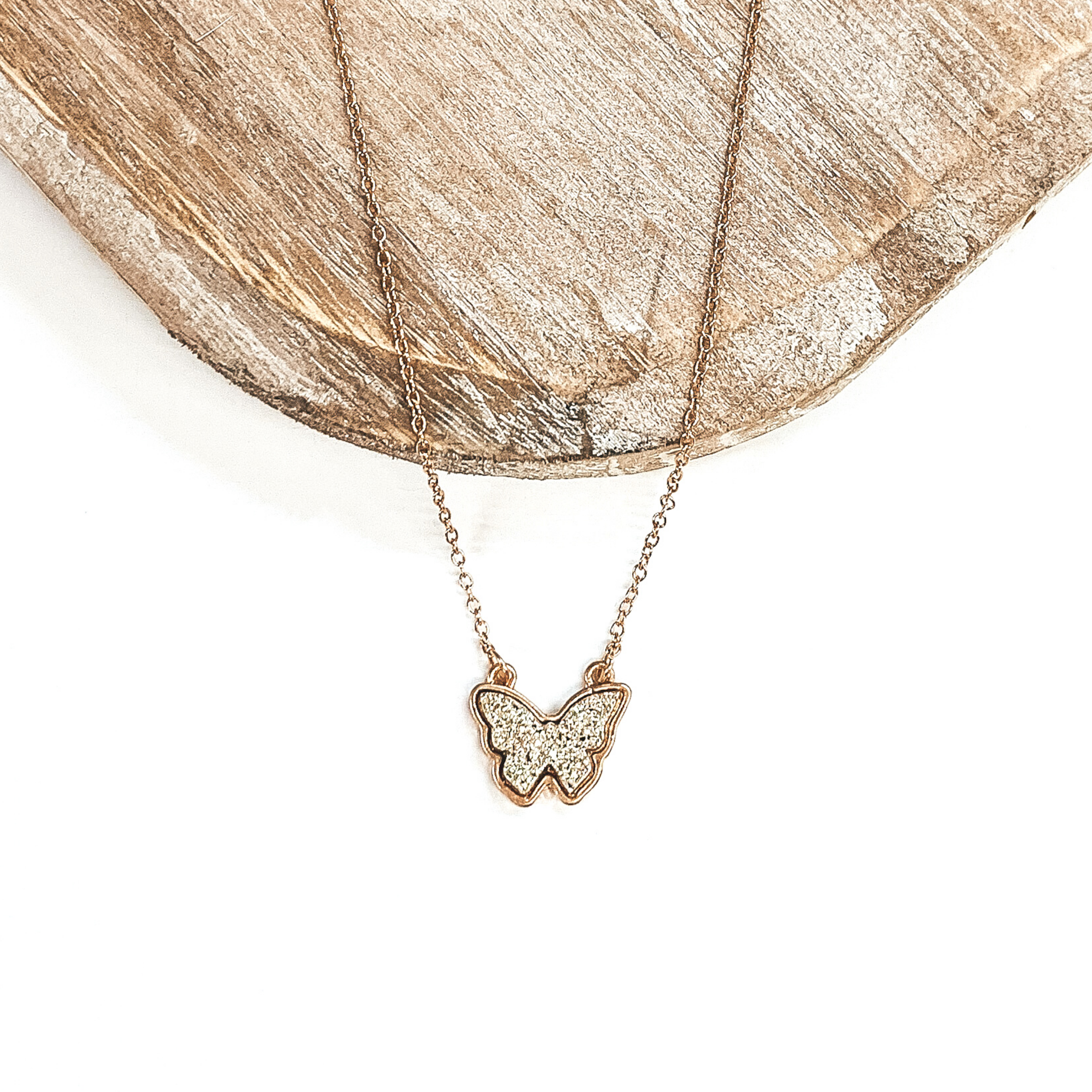 Gold necklace with white gold druzy butterfly pendant. Pictured on a white and brown background.