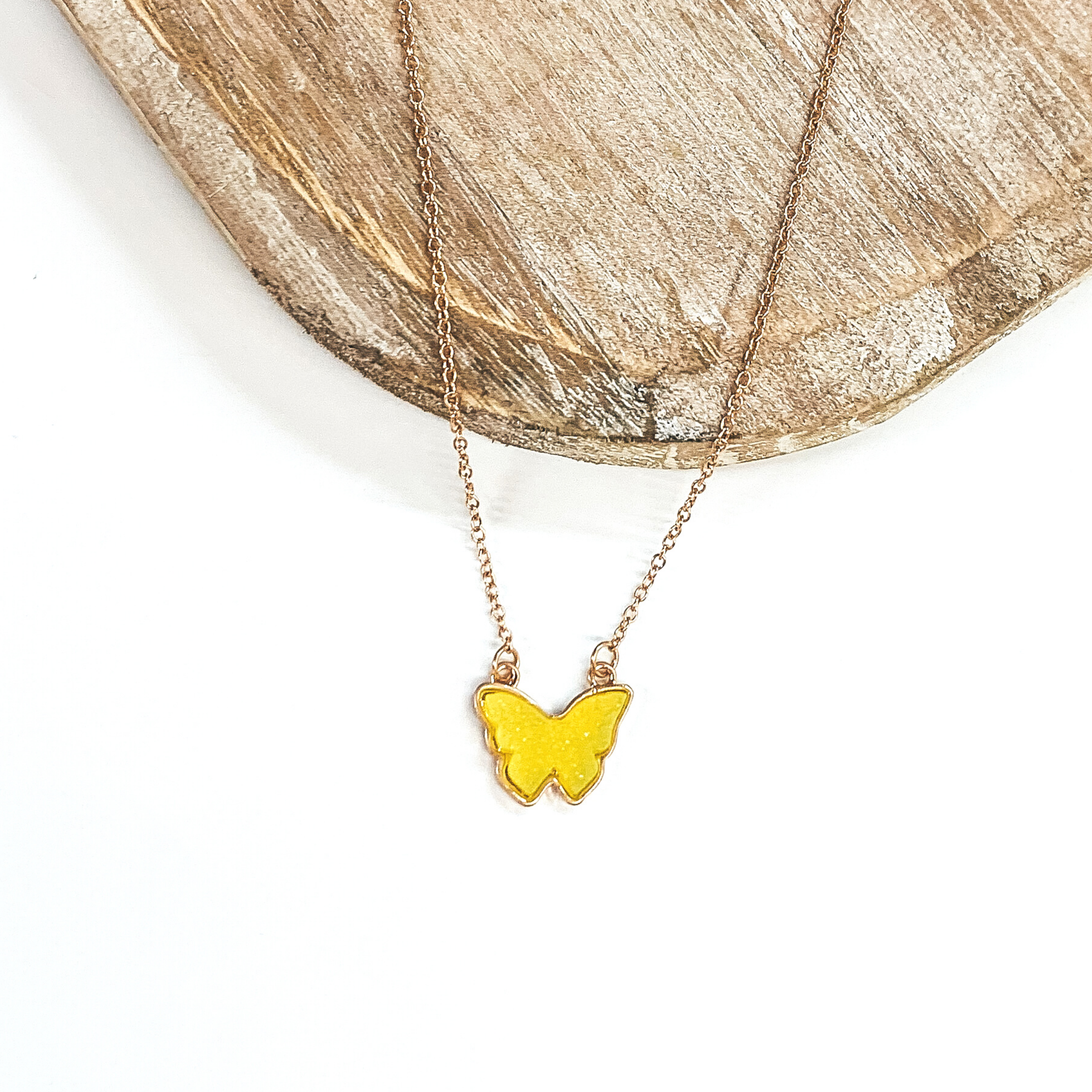Gold necklace with neon yellow druzy butterfly pendant. Pictured on a white and brown background.