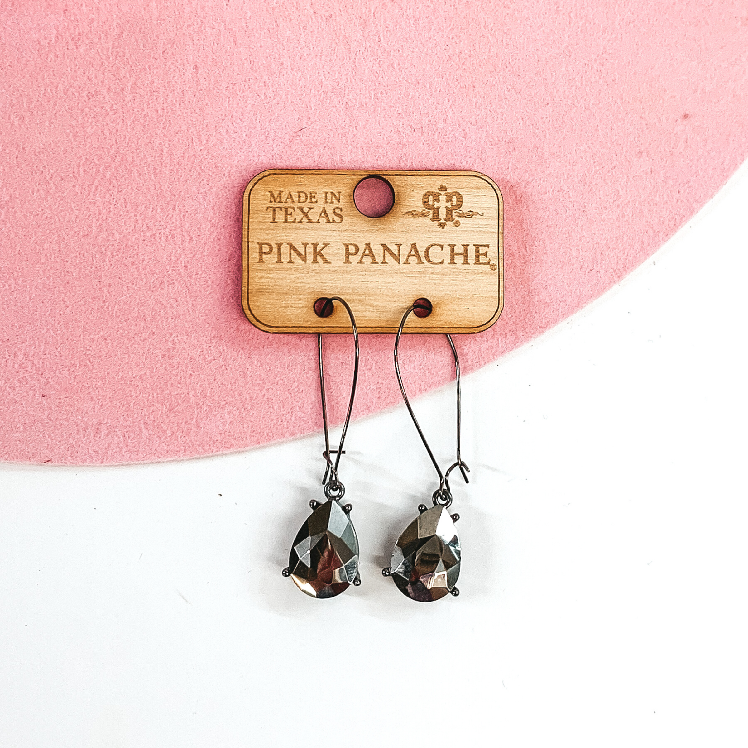 Thin black wire earrings with a hanging teardrop crystal in the color jet hematite. These earrings are pictured on a wood Pink Panache earrings holder on a white and pink background. 