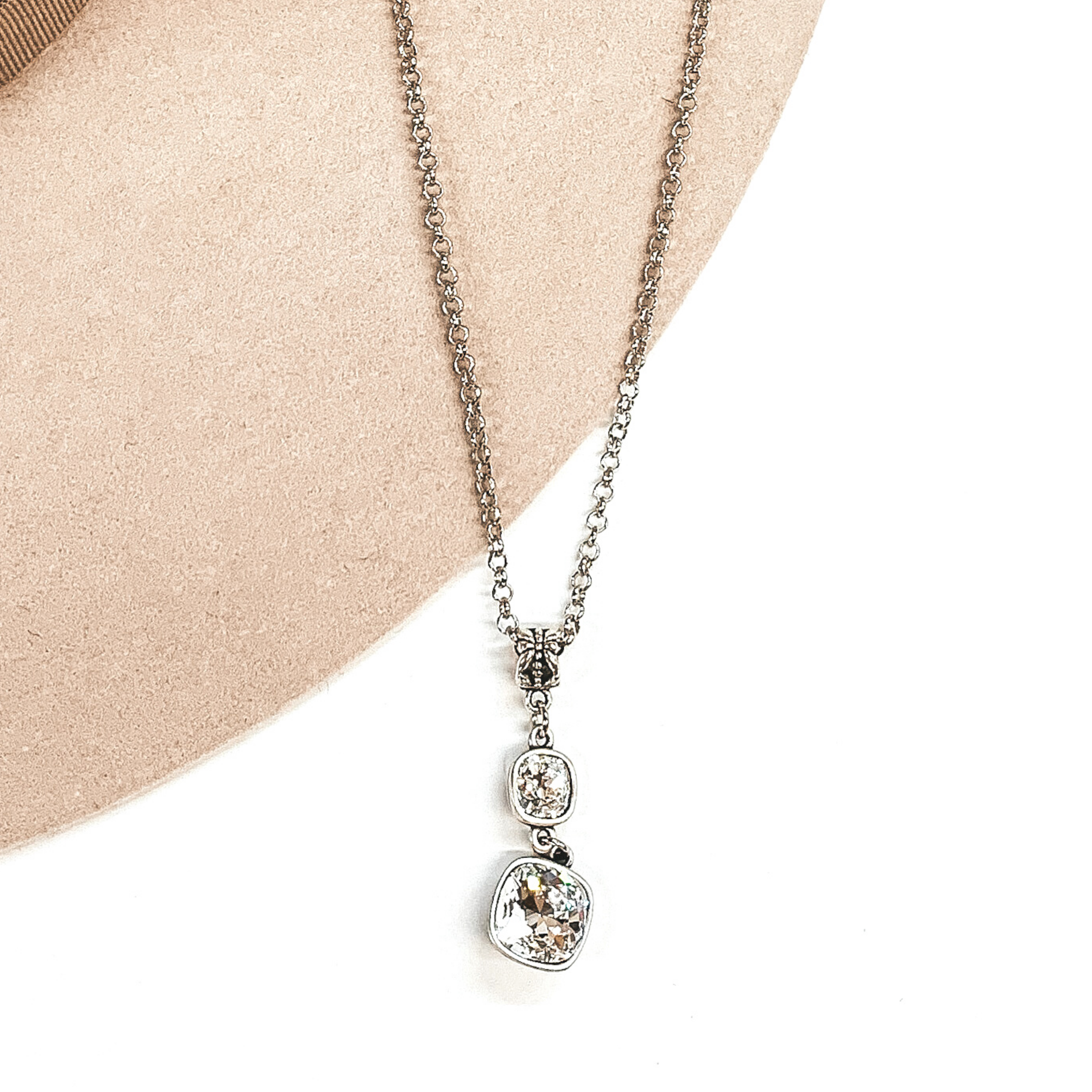 Silver adjustable chained necklace with a two clear square stone pendant on a white and beige background
