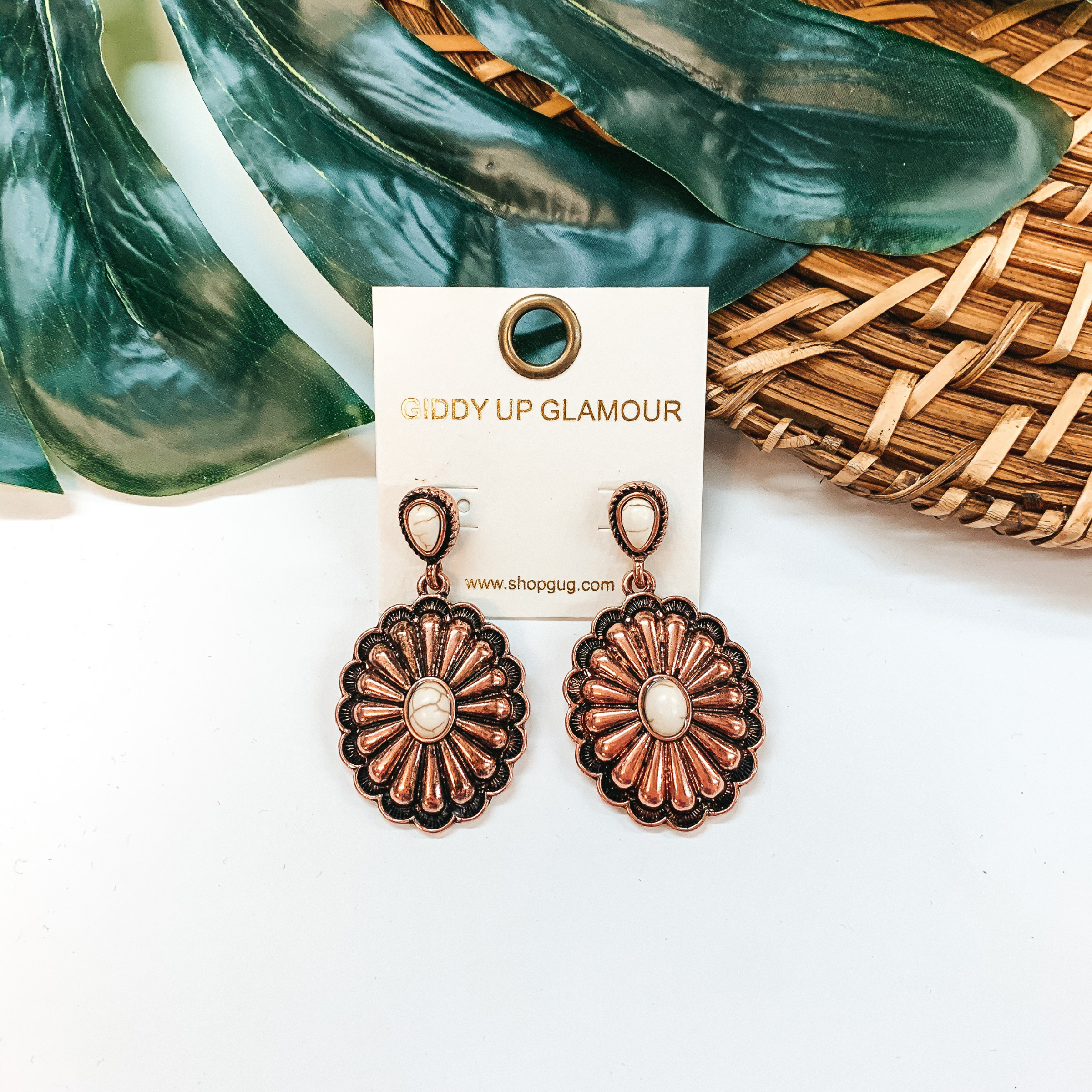 A pair of copper concho earrings with ivory stones. These earrings are pictured on a white background with a basket and palm leaf.