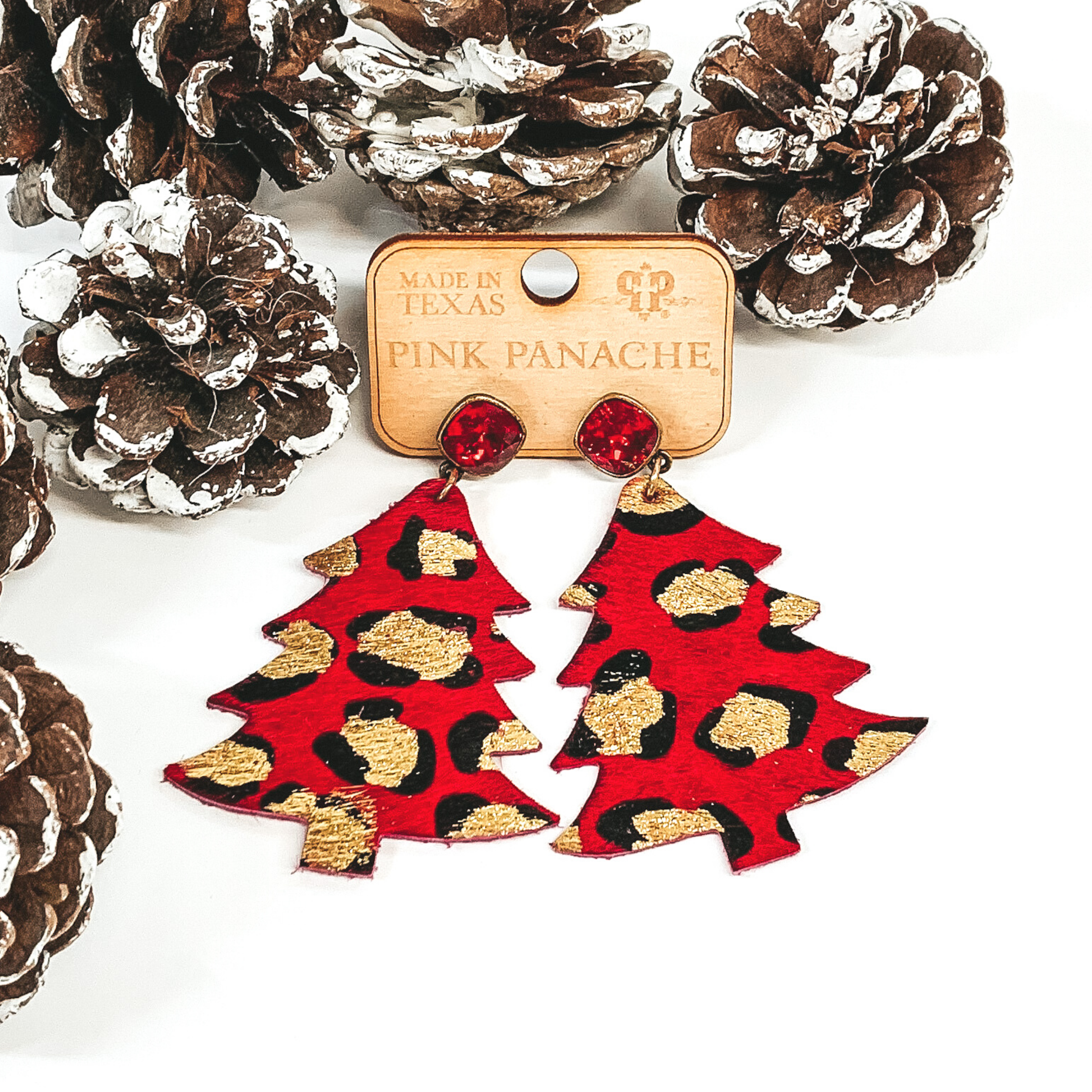 Red square crystal studs with a red and gold leopard Christmas tree pendant hanging from the bottom. Pictured on a a white background with pine cones. 