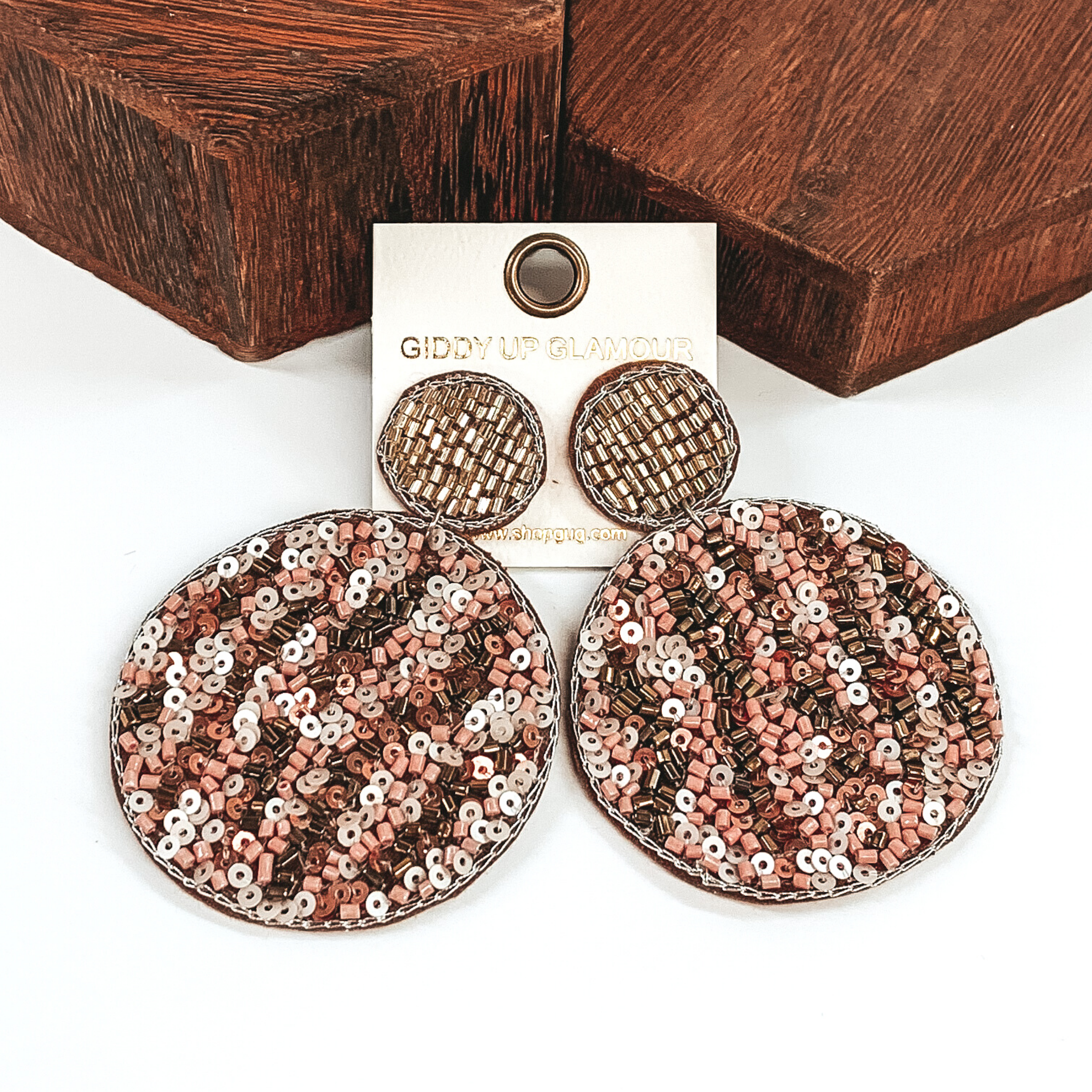 The studs are a small beaded circle with a hanging larger beaded circle. These beaded earrings includes the colors ivory, nude, light pink, and gold in a leopard design. These earrings are pictured on a white background with brown blocks behind the earrings.