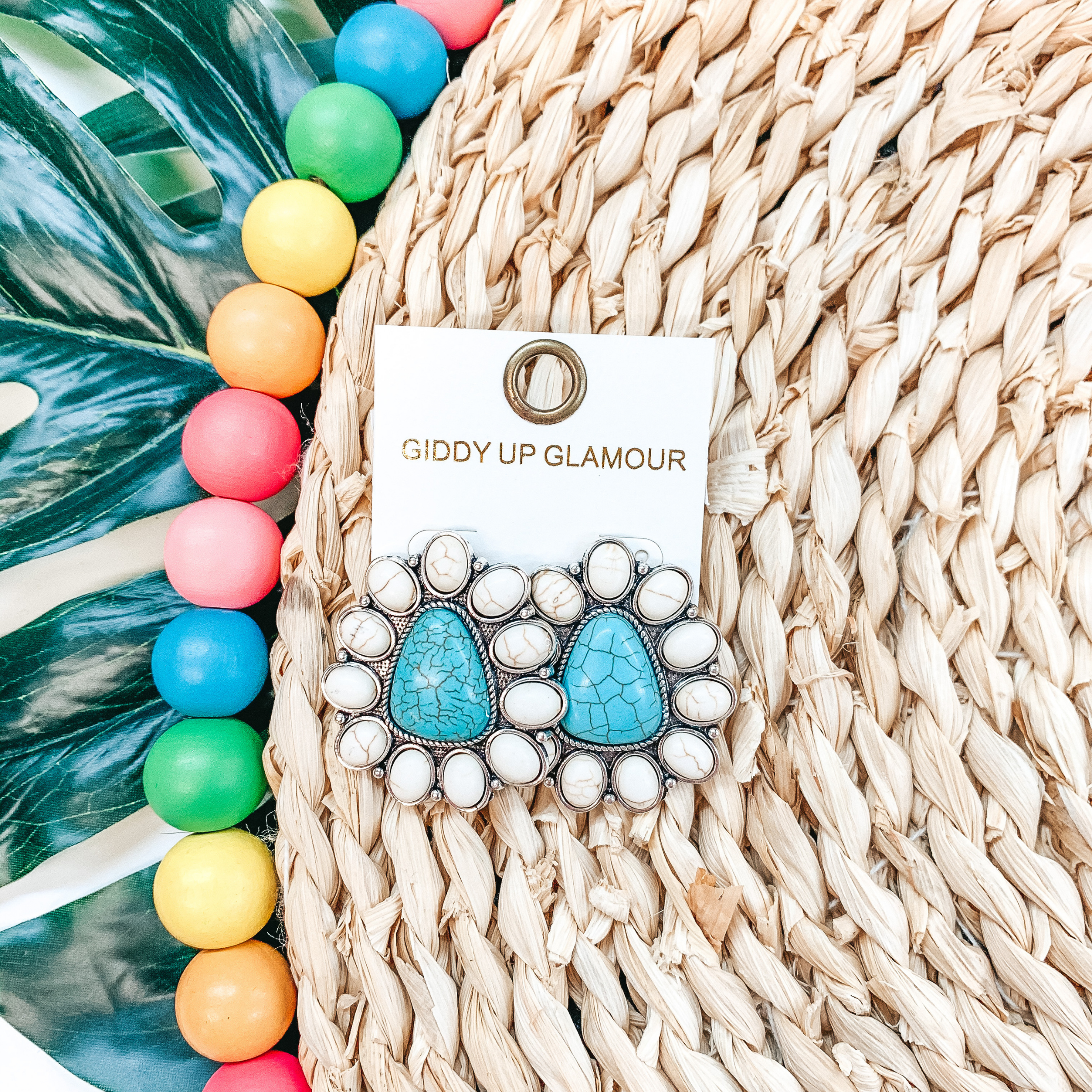 Triangle cluster earrings with white stones and a center turquoise stone. These earrings are pictured on top of a tan basket weave and multicolor beads. 