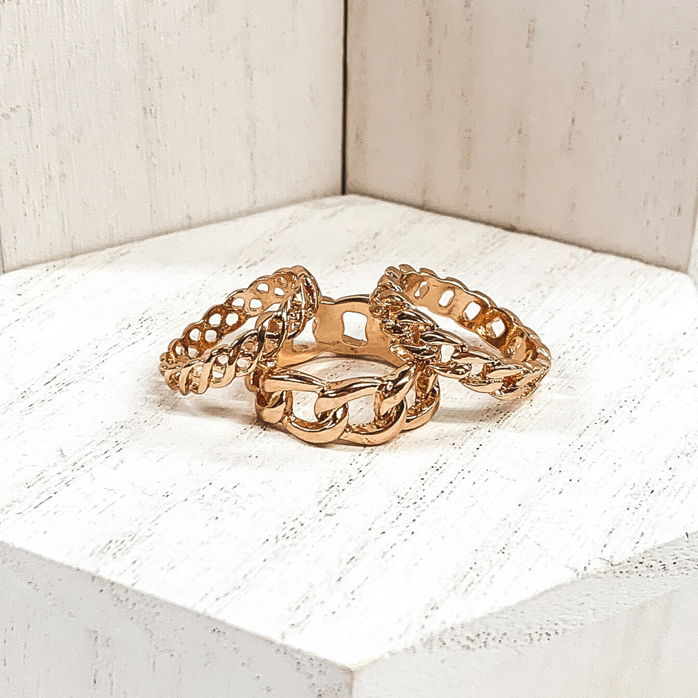 This set of gold rings include three different band widths and different types of chains for each ring. These rings are pictured on a white background.