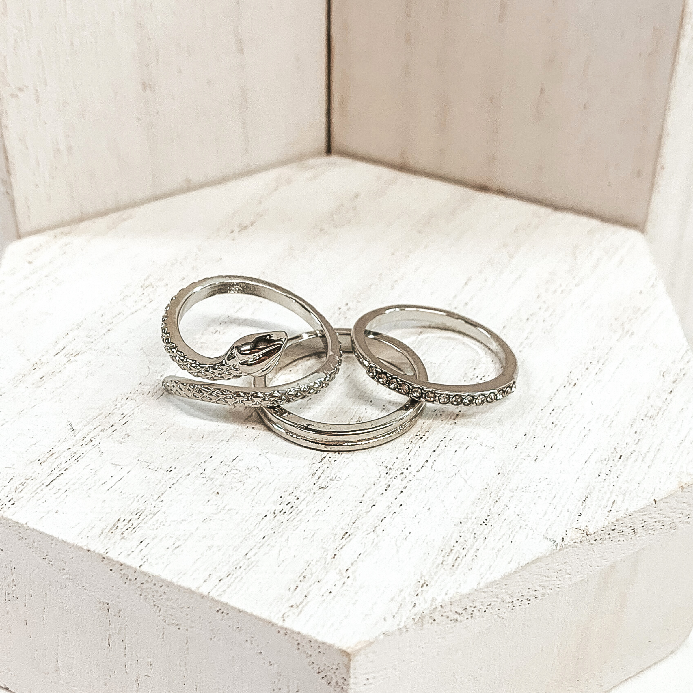 This silver ring set is very edgy. It includes one snake ring, one double layered ring, and one ring with a row of crystals. These rings are pictured on a white background.