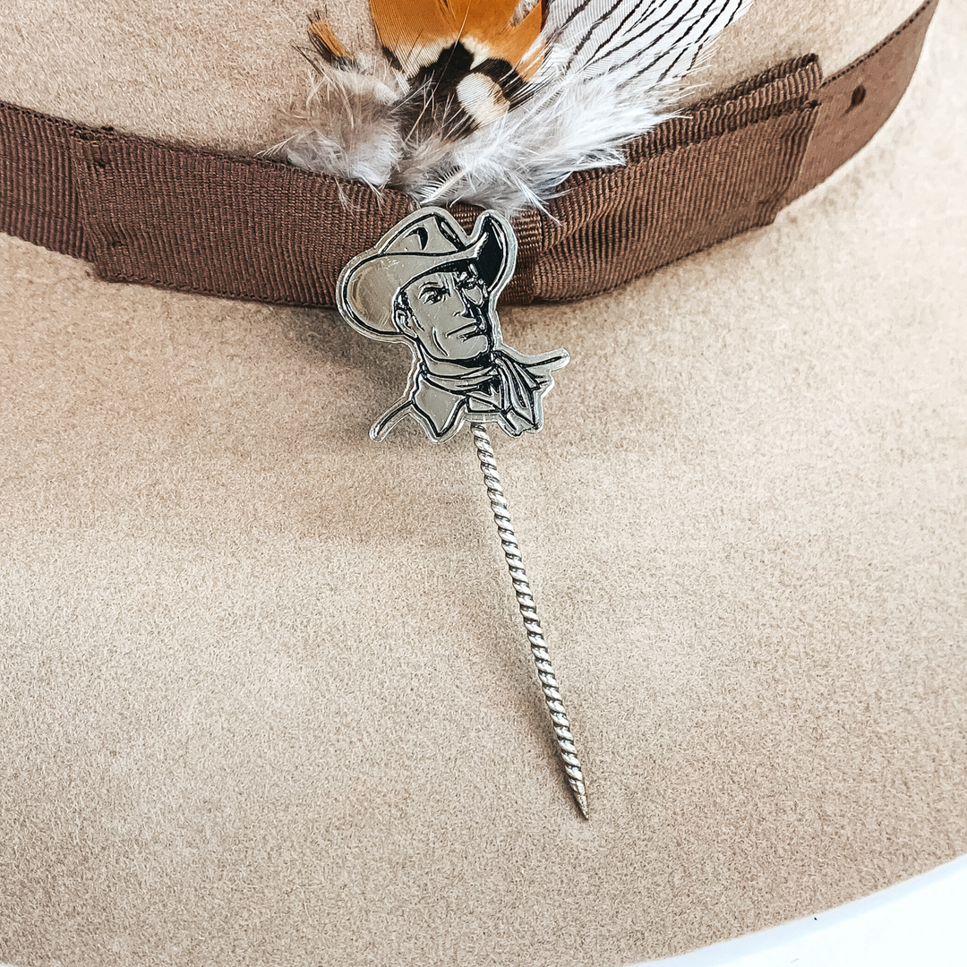 Silver twisted toothpick hat pin with a silver pendant of a cowboy's face. The pendant includes a hat on the boys head. This hat pin is pictured on a tan hat.