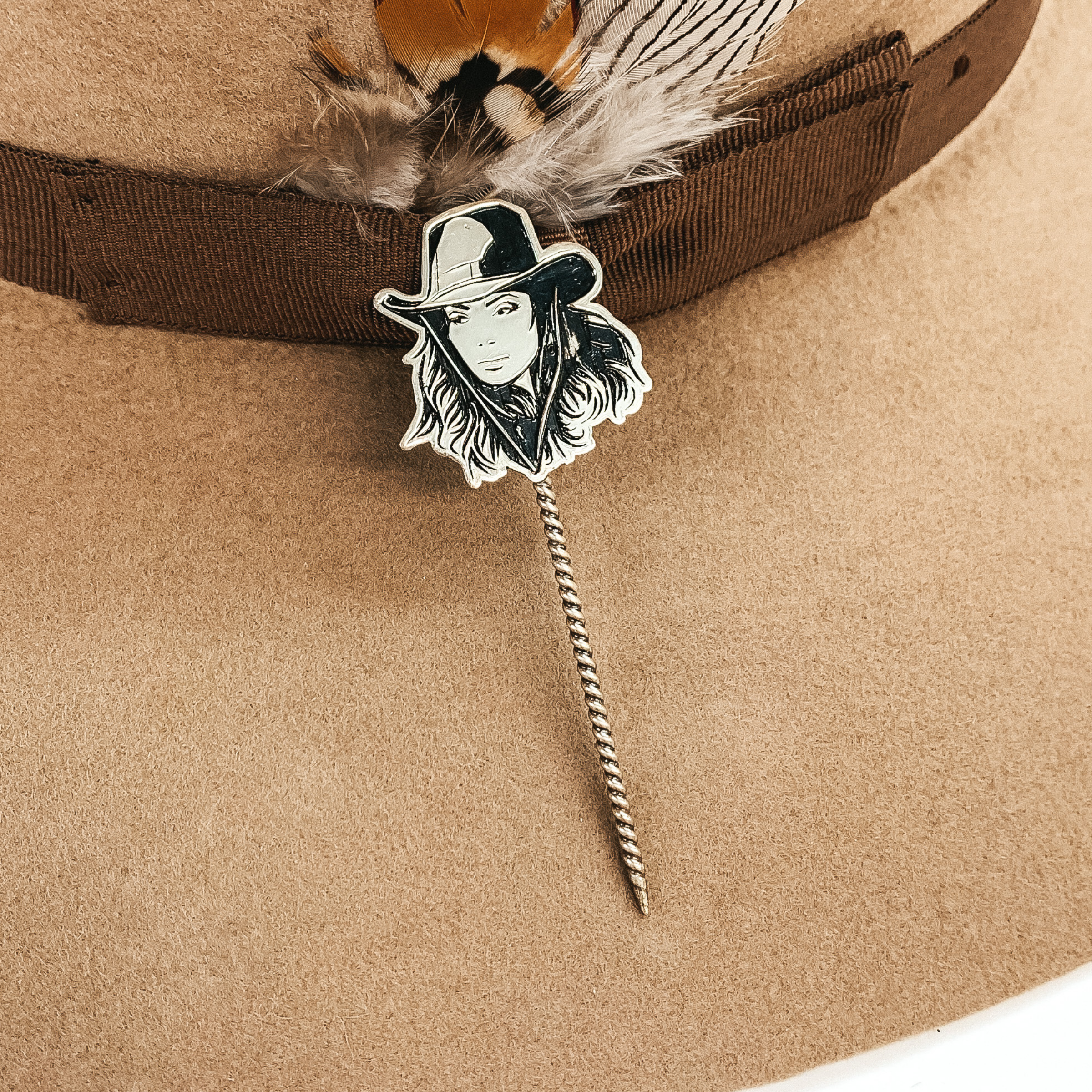 Silver twisted toothpick hat pin with a silver pendant of a cowgirl's face. The pendant includes a hat on the girls head. This hat pin is pictured on a tan hat.