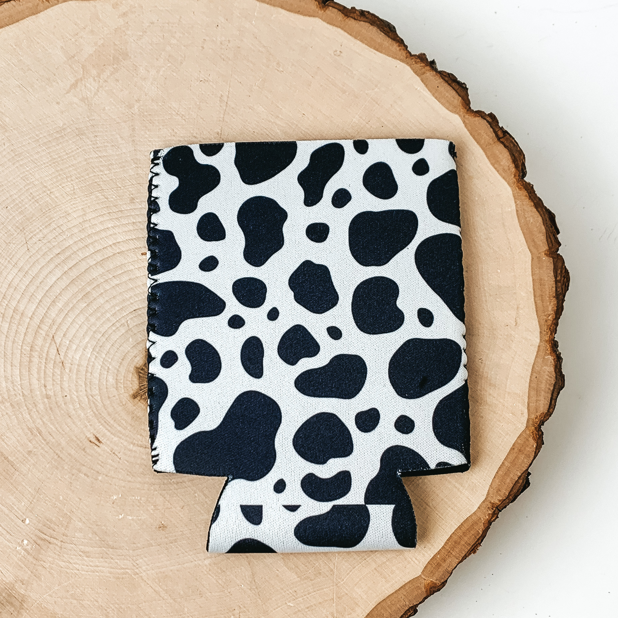 This Black and White cow print kooozie is pictured on a peice of wood, with a white background.  