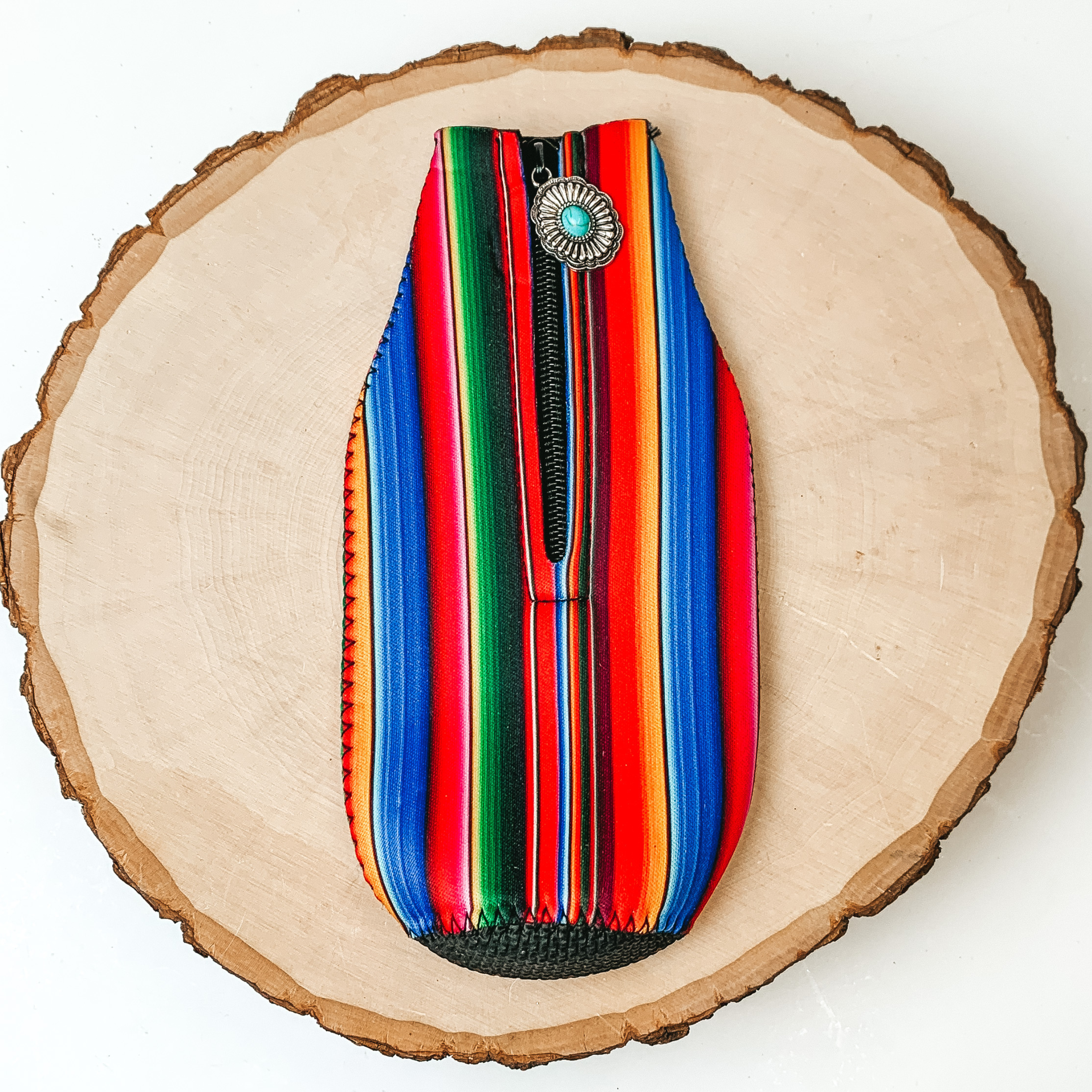 This Serape Zip Up Print kooozie With Concho Charm is pictured on a peice of wood, with a white background.  