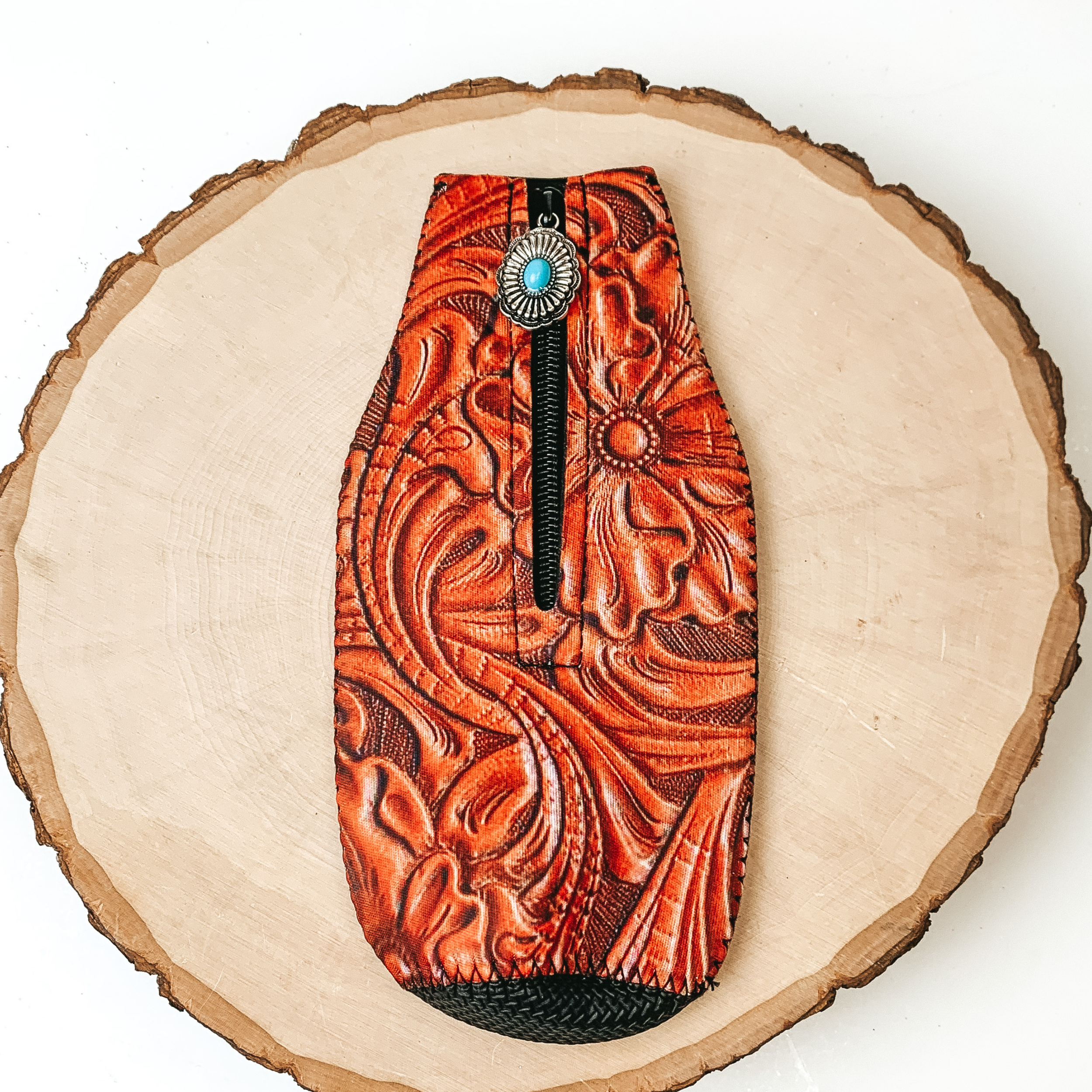 This Leather Tooled Print Zip Up kooozie With a Concho Charm is pictured on a peice of wood, with a white background.  