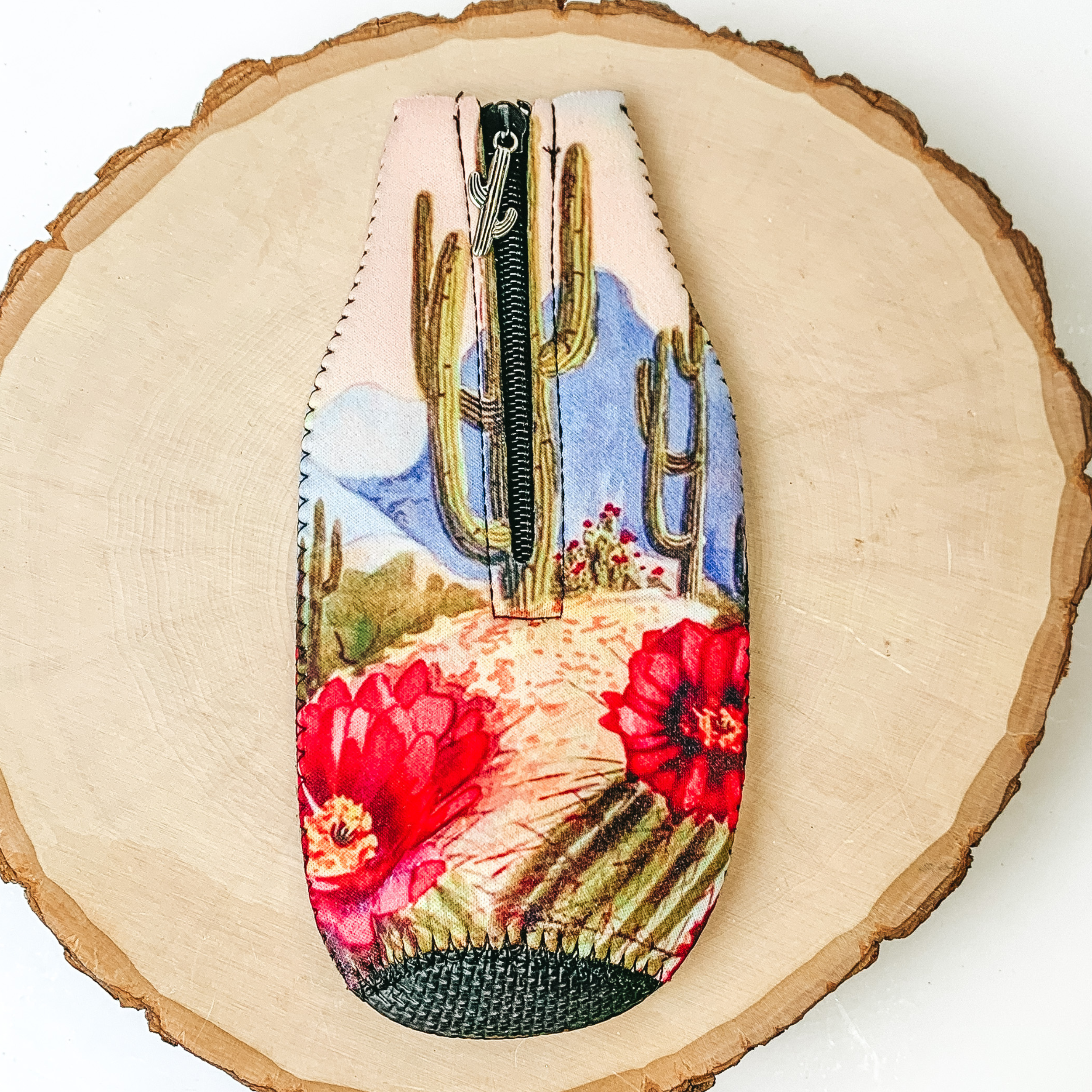 This Cactus Landscape Zip Up kooozie With a Cactus Charm is pictured on a peice of wood, with a white background.  