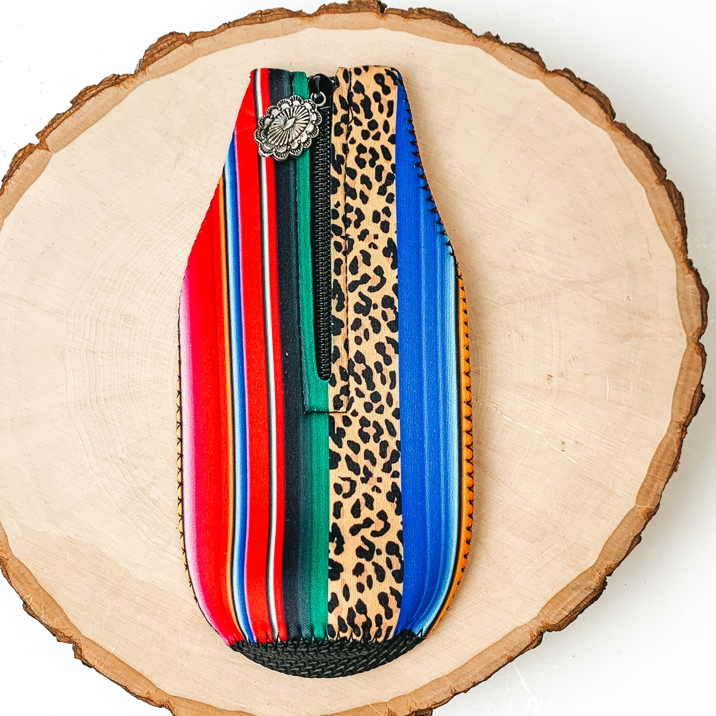 This Serape and Leopard Print Stripe Zip Up kooozie With Concho Charm is pictured on a peice of wood, with a white background.  