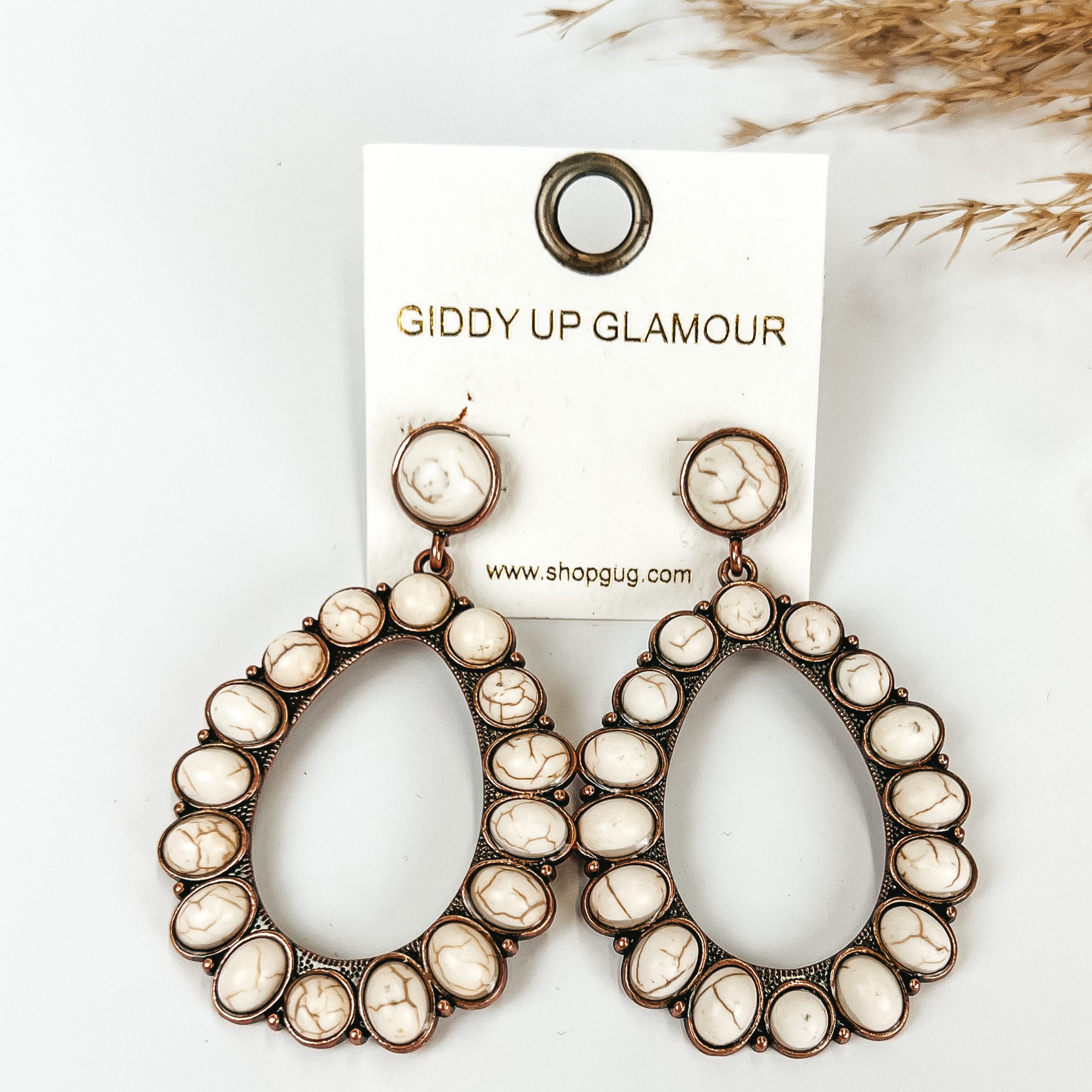 White stoned teardrop earrings, with pompous grass in the top right hand corner, on a white background.