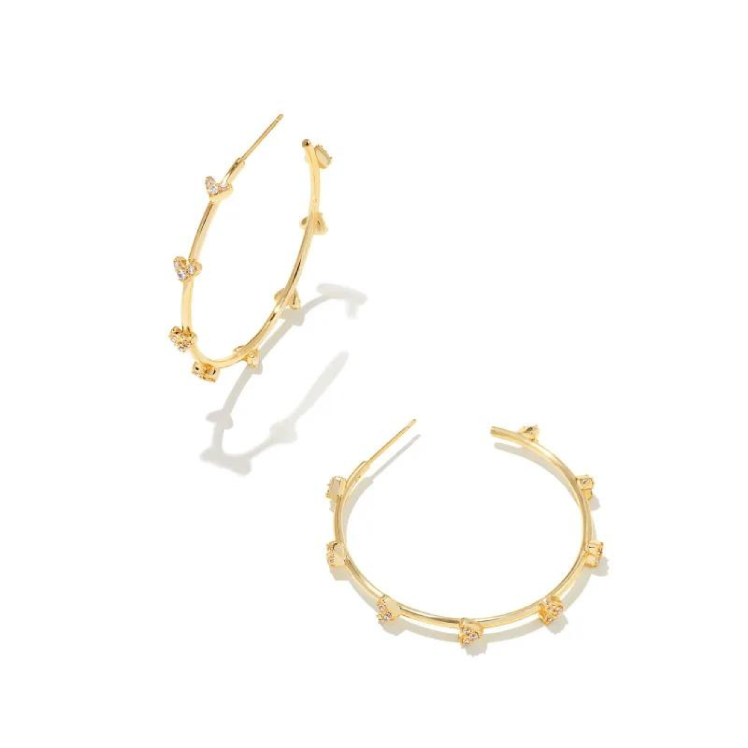 Gold hoop earrings with white crystal hearts pictured on a white background. 