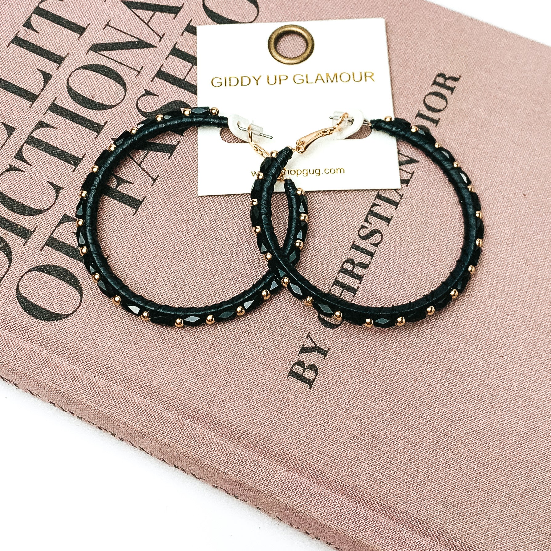 Pictured are circle beaded hoop earrings with gold spacers in black. They are pictured with a pink fashion journal on a white background