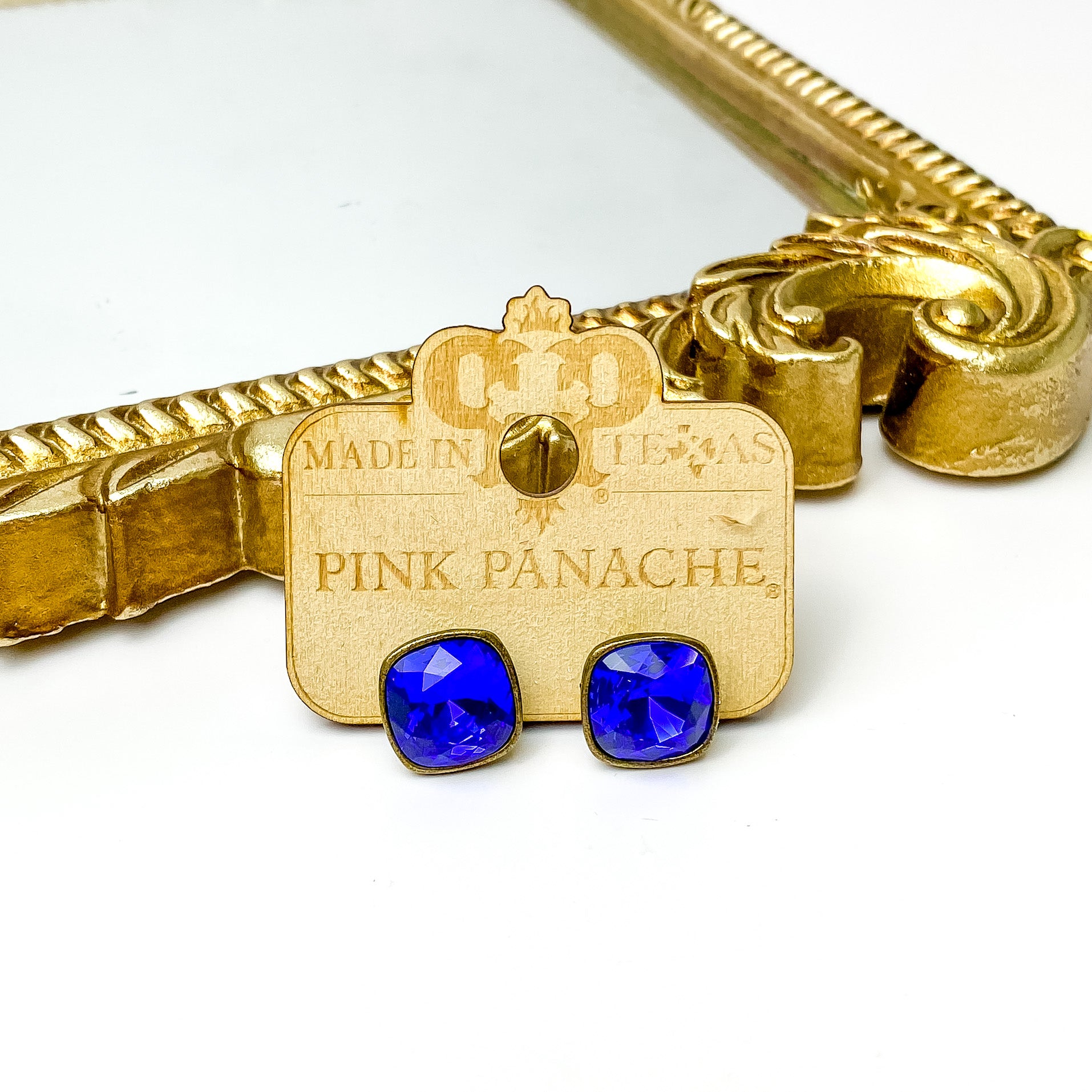 Majestic blue cushion cut crystal stud earrings with a silver setting. These earrings are pictured on a Pink Panache wood holder in front of a gold mirror and on a white background.